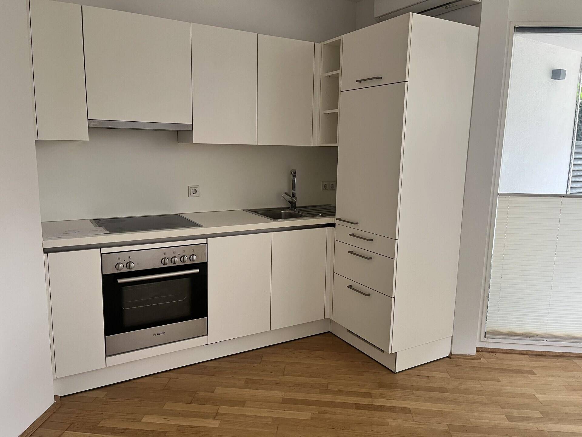 Moderne Einbauküche mit weißen Schränken, integriertem Backofen und viel Stauraum.