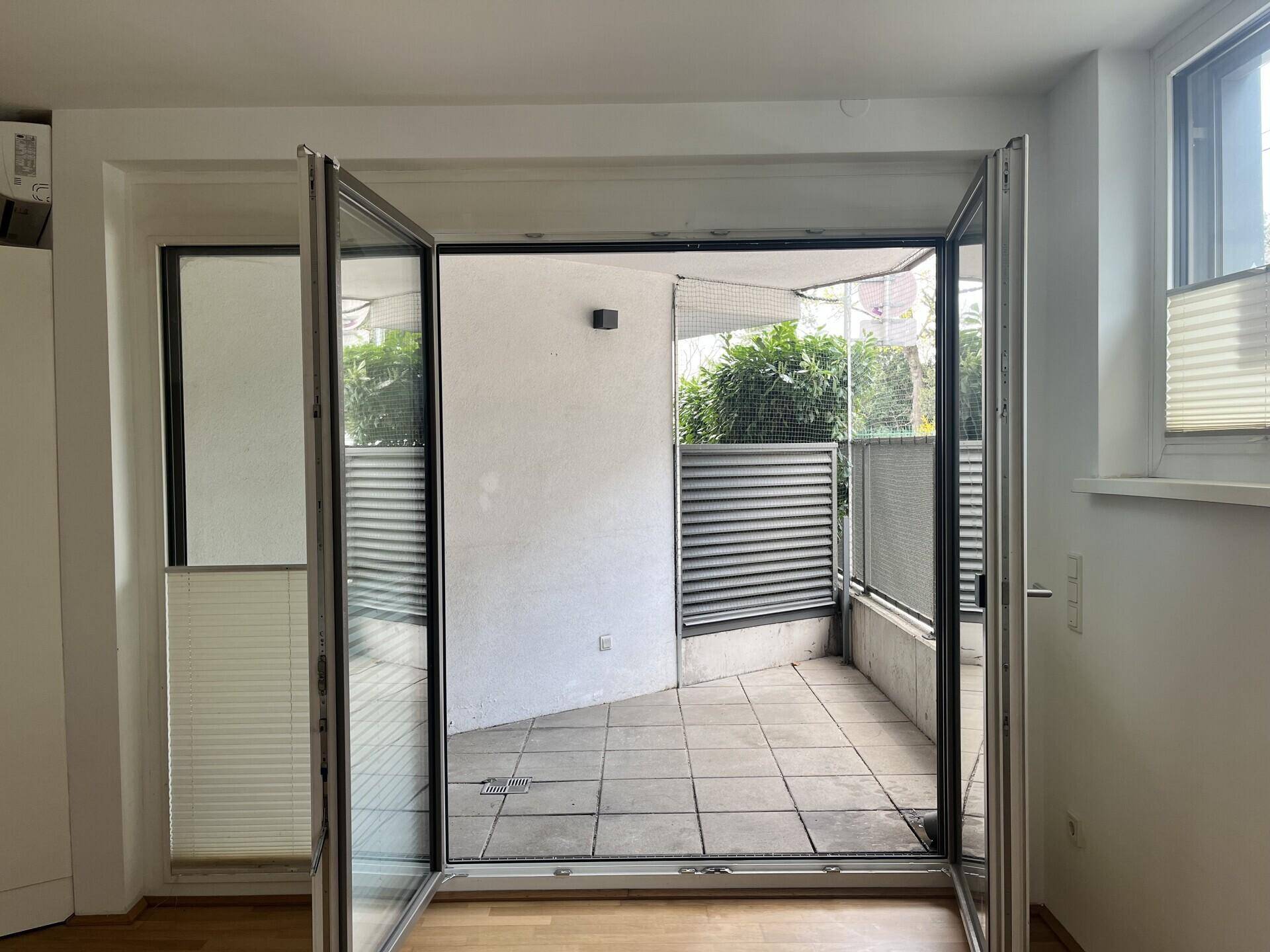 Blick vom Innenraum auf die geflieste Terrasse mit Sichtschutz und viel Tageslicht.