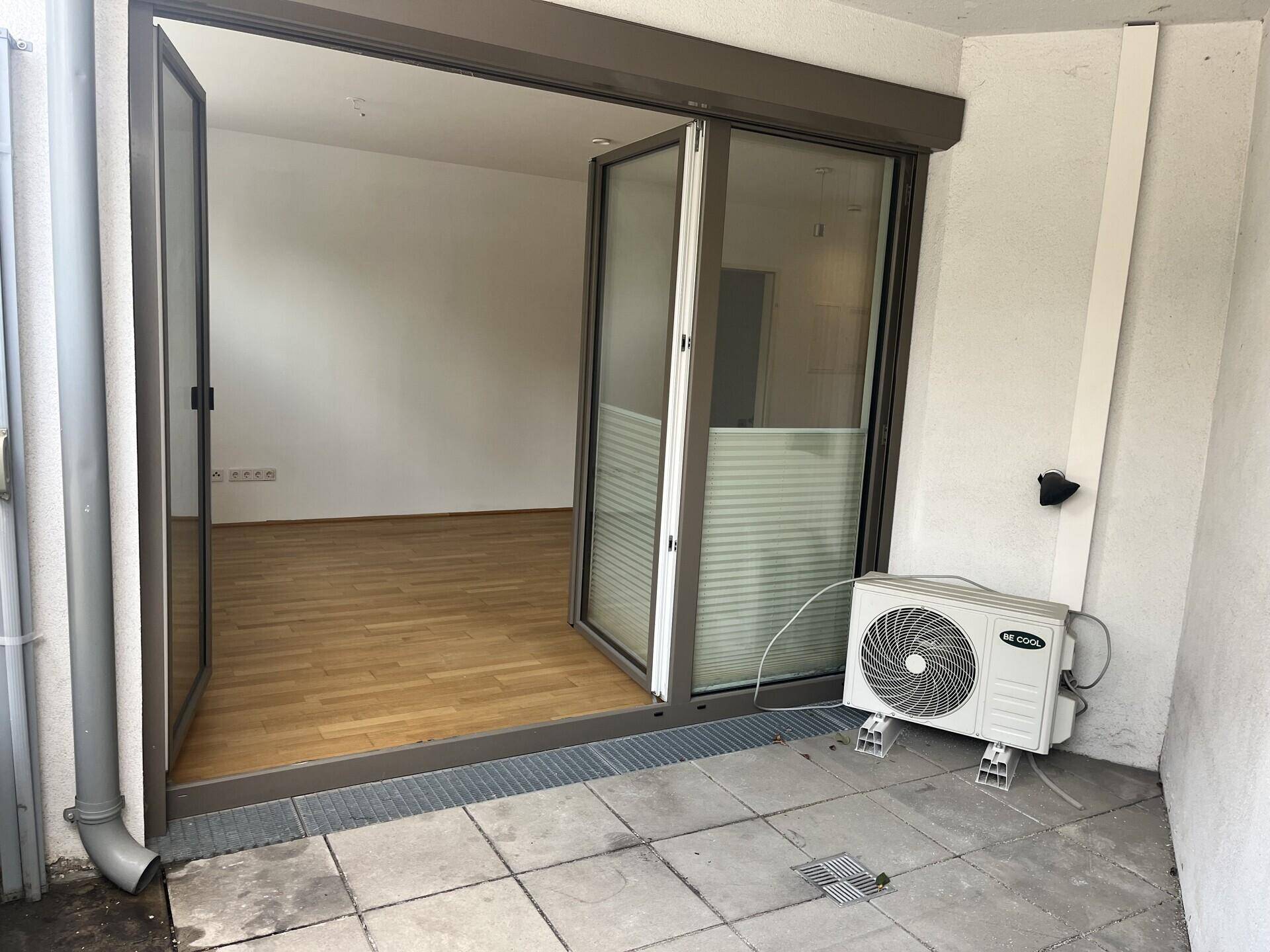 Geflieste Terrasse mit Klimaanlage-Außengerät und Zugang zum Wohnbereich.
