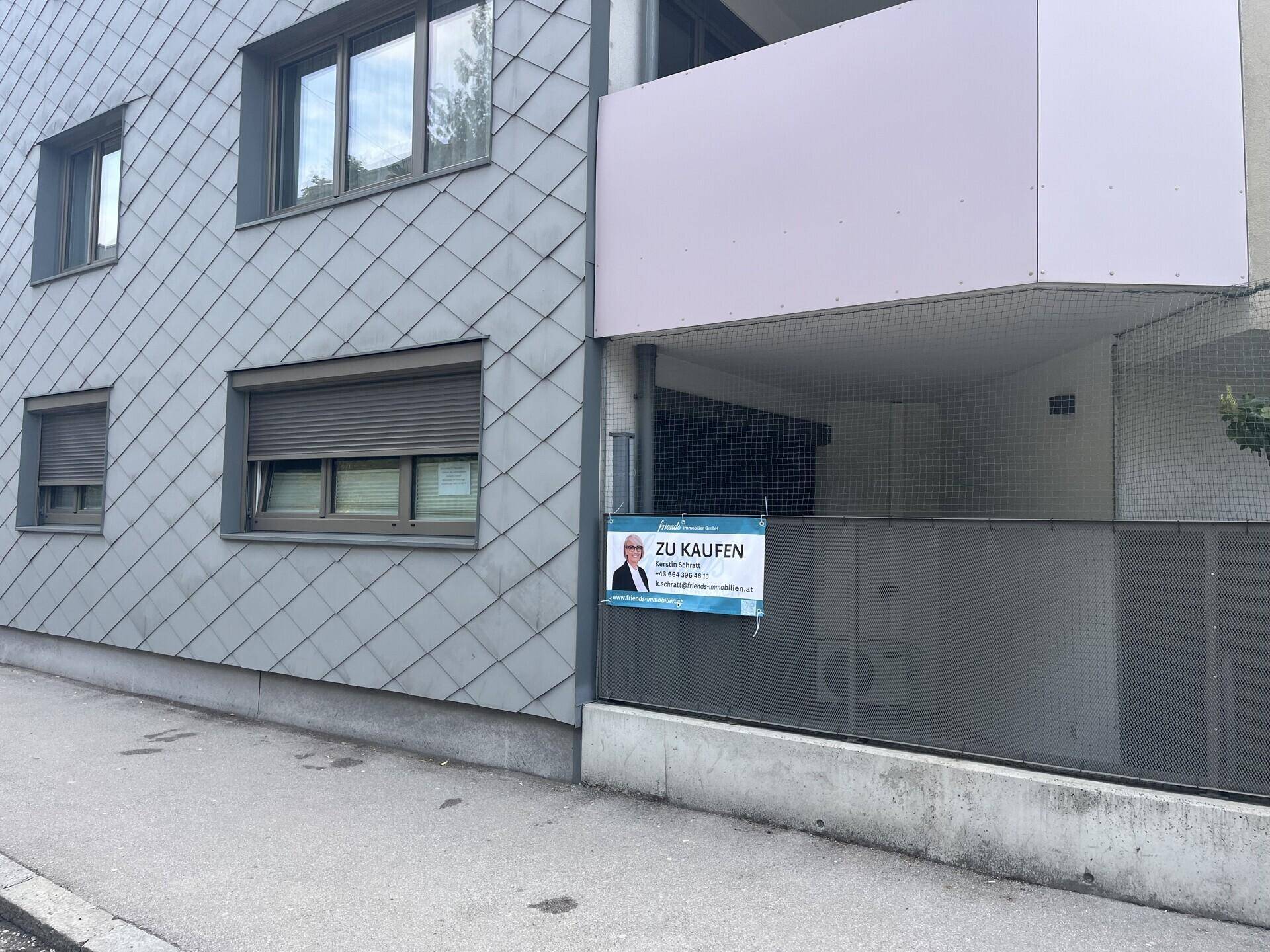 Außenansicht des Gebäudes mit "Zu Kaufen" Schild und Rollläden an den Fenstern.