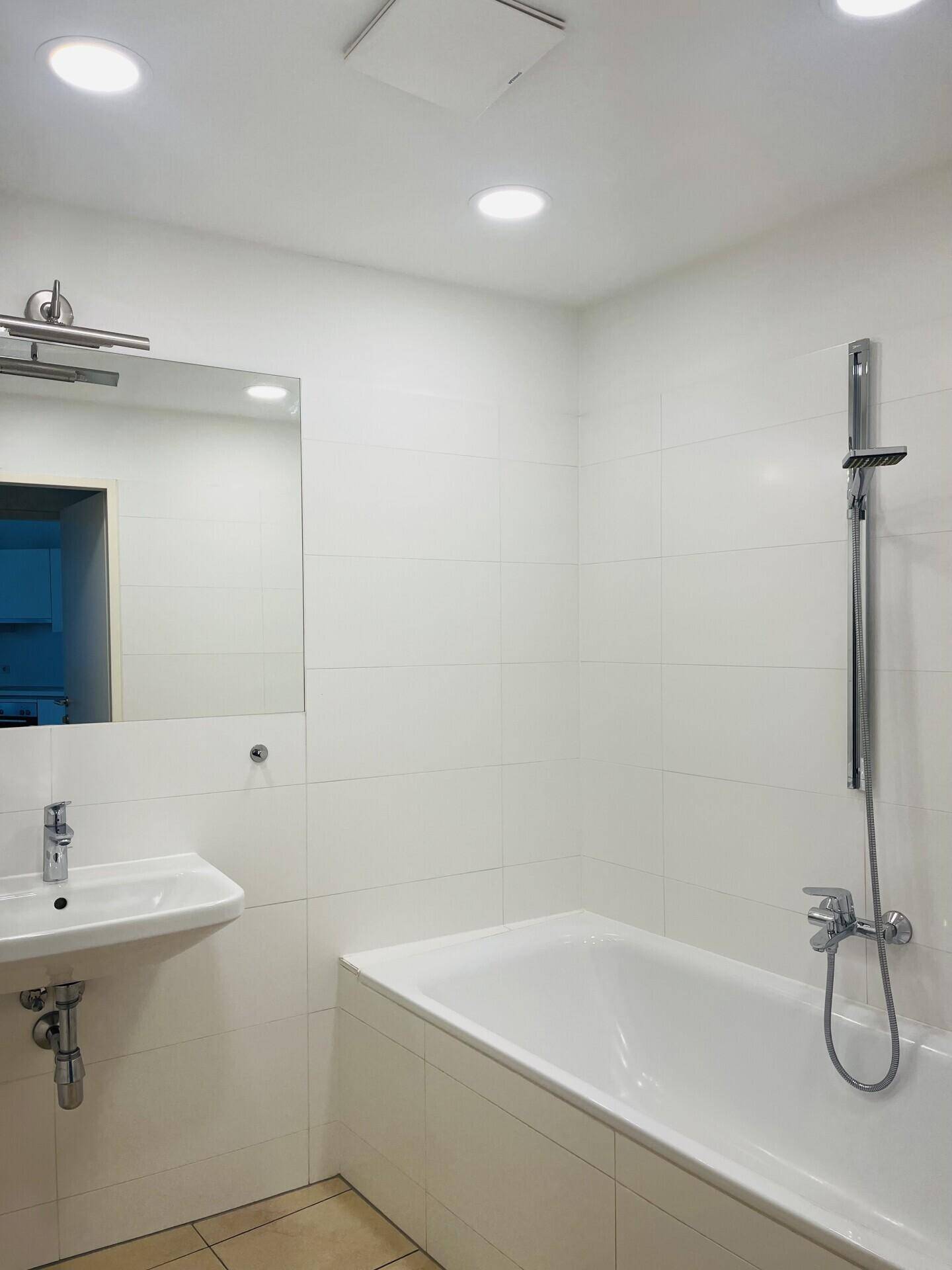 Modernes Badezimmer mit Badewanne, Duscharmatur und weiß gefliesten Wänden.