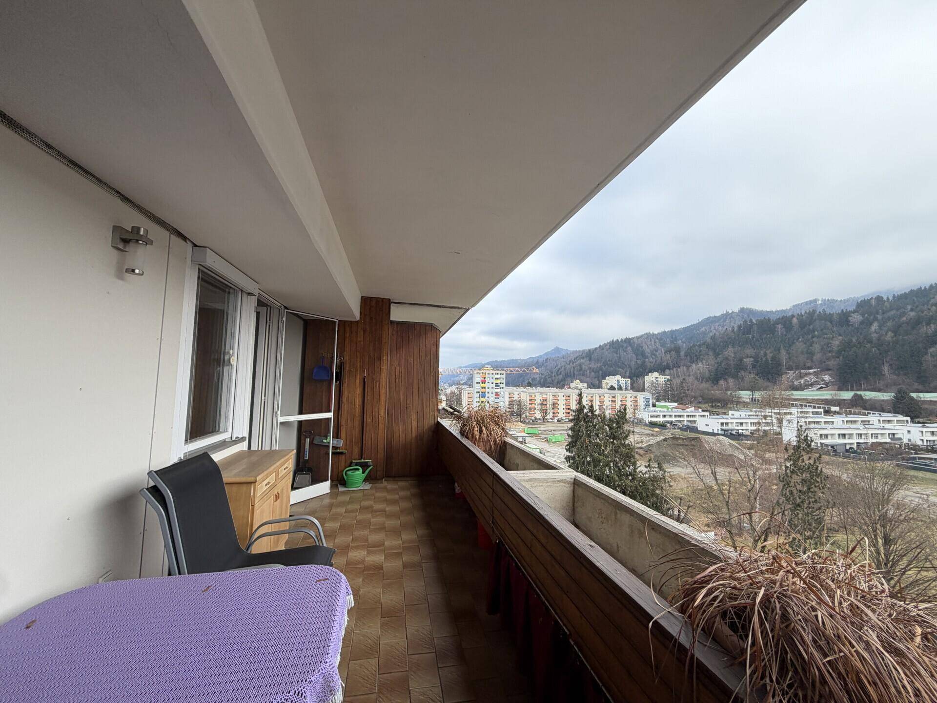 Breiter Balkon mit Fliesenboden, Holzelementen und weitem Blick auf die Landschaft.