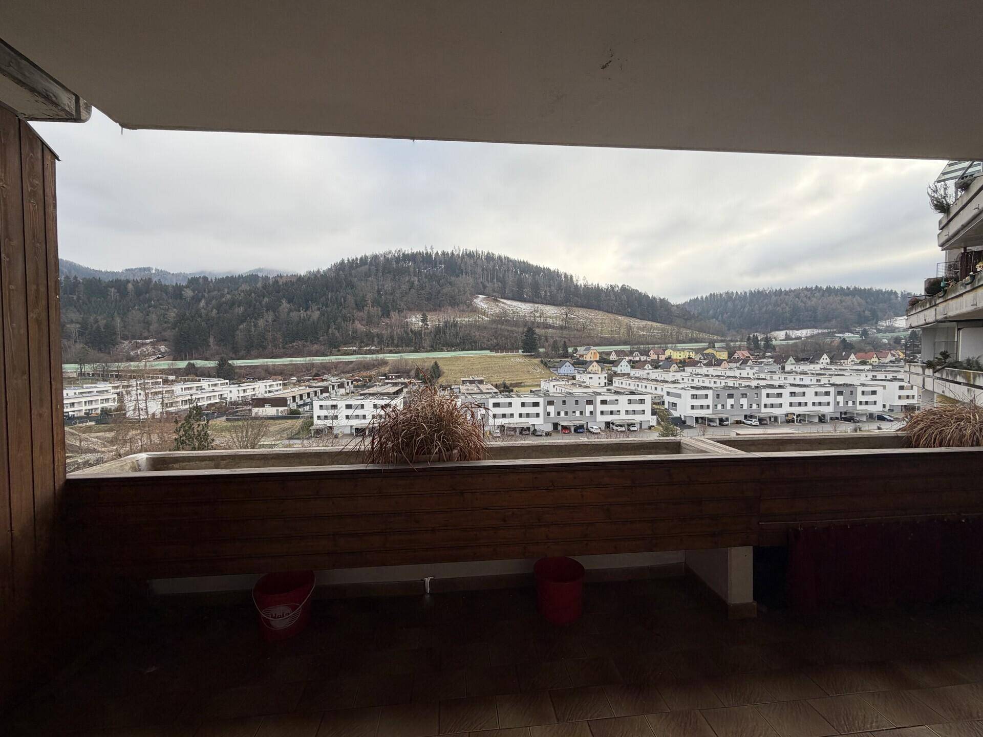 Großer Balkon mit Panoramablick auf die umliegende Hügellandschaft und Wohngebäude.