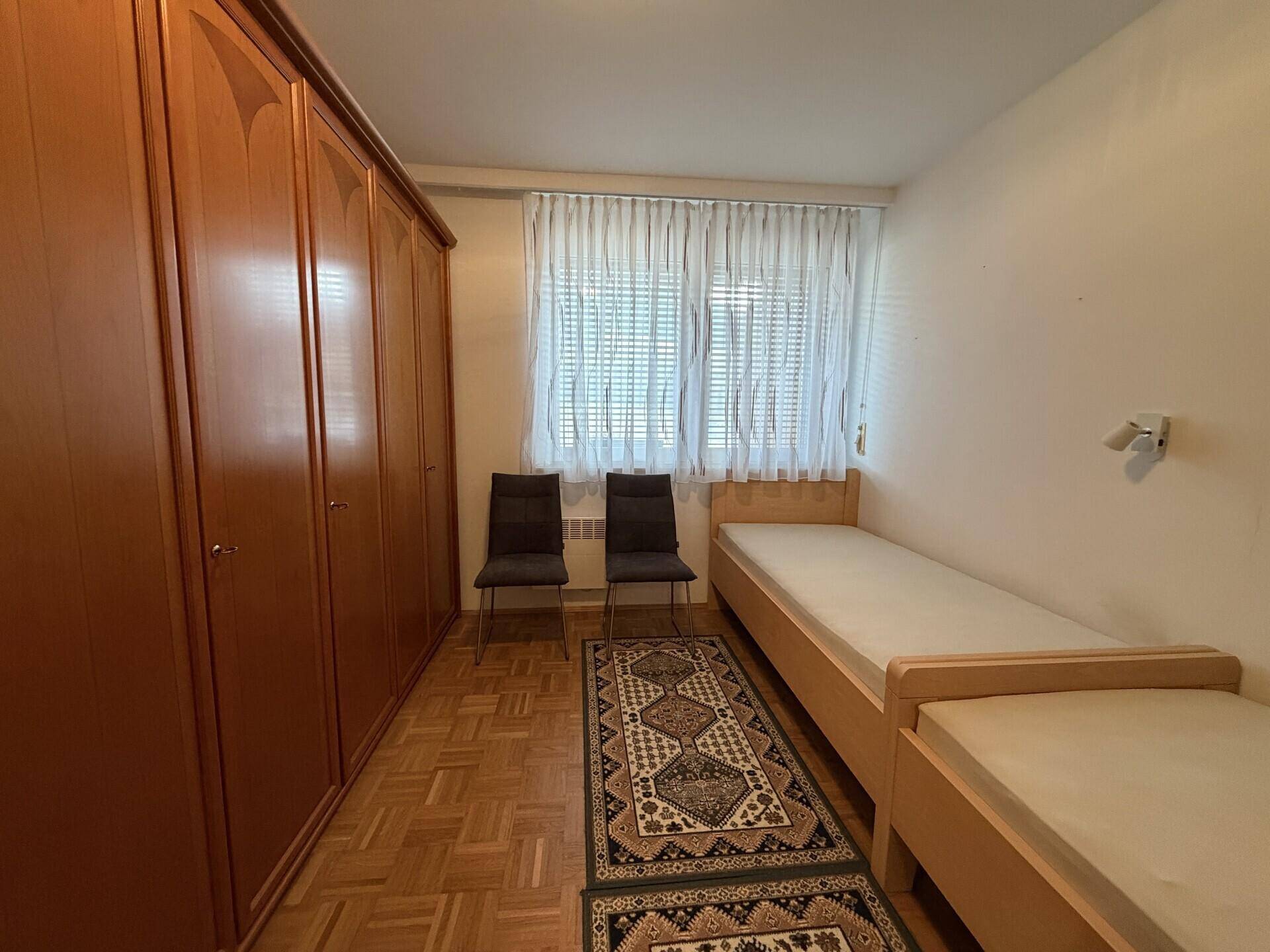 Schlafzimmer mit zwei Einzelbetten, großem Kleiderschrank und Fenster mit Vorhängen.