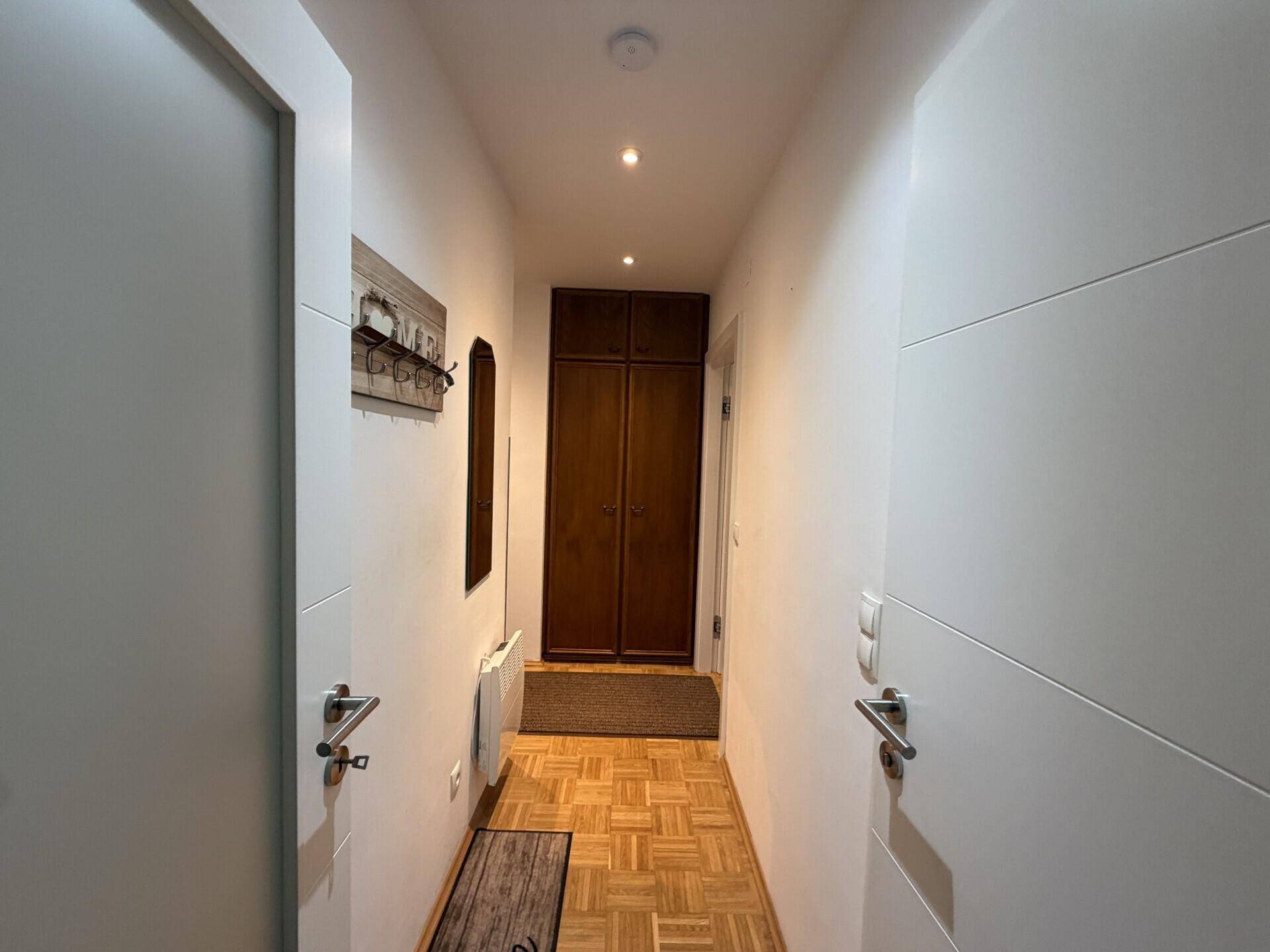 Schmaler Flur mit Parkettboden, Einbauschrank und weiß gestrichenen Wänden.