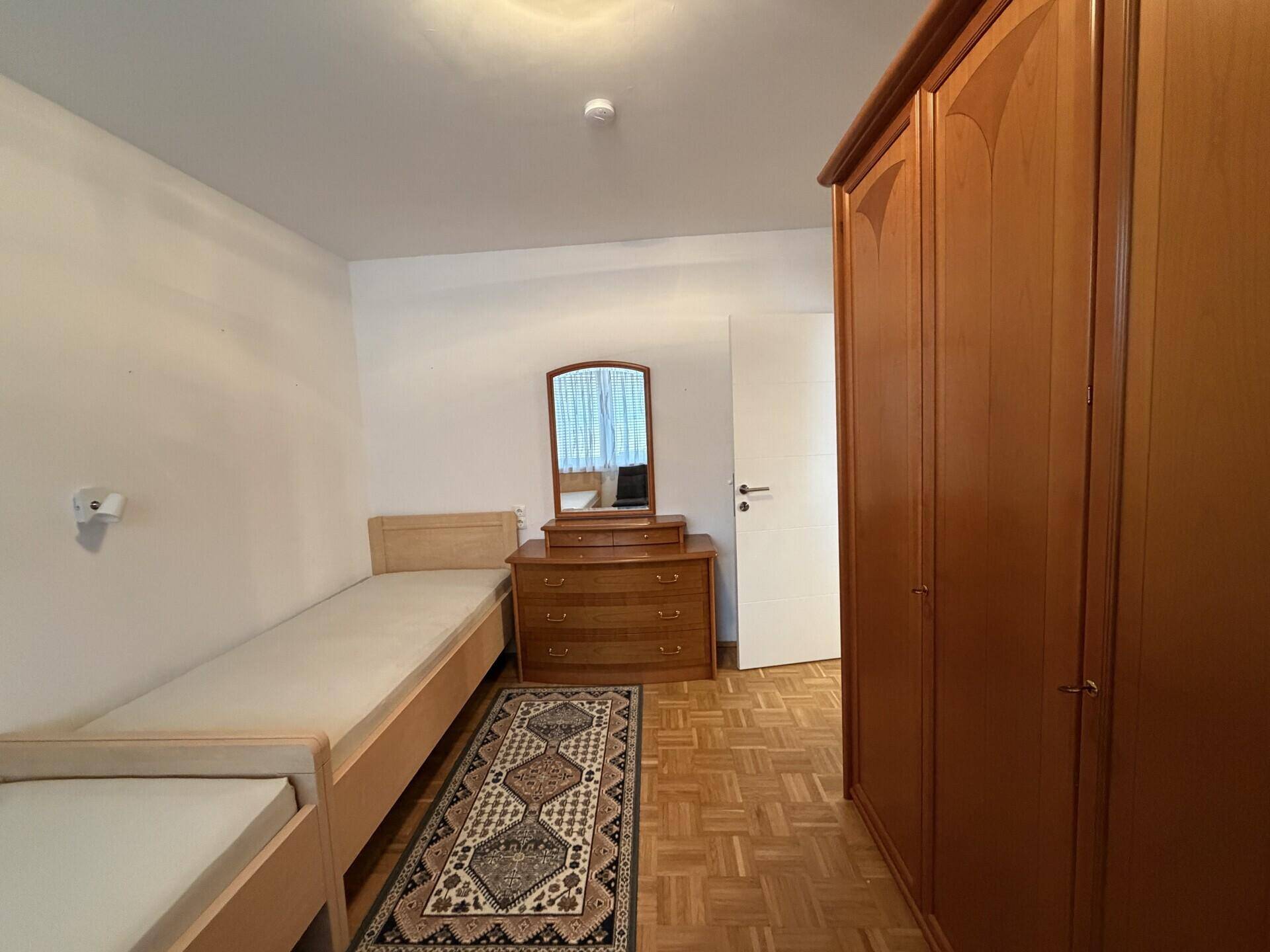 Schlafzimmer mit zwei Einzelbetten, Holzschrank und Parkettboden.