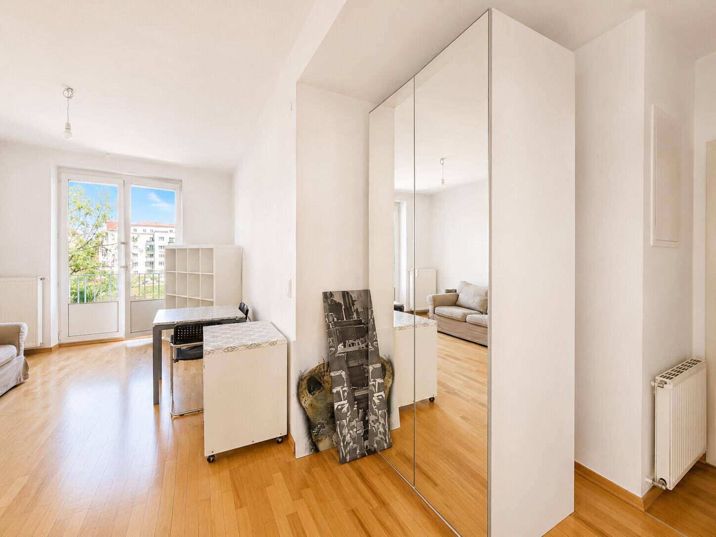 Heller Wohnbereich mit Parkettboden und Spiegelschrank, der zum Balkon führt.