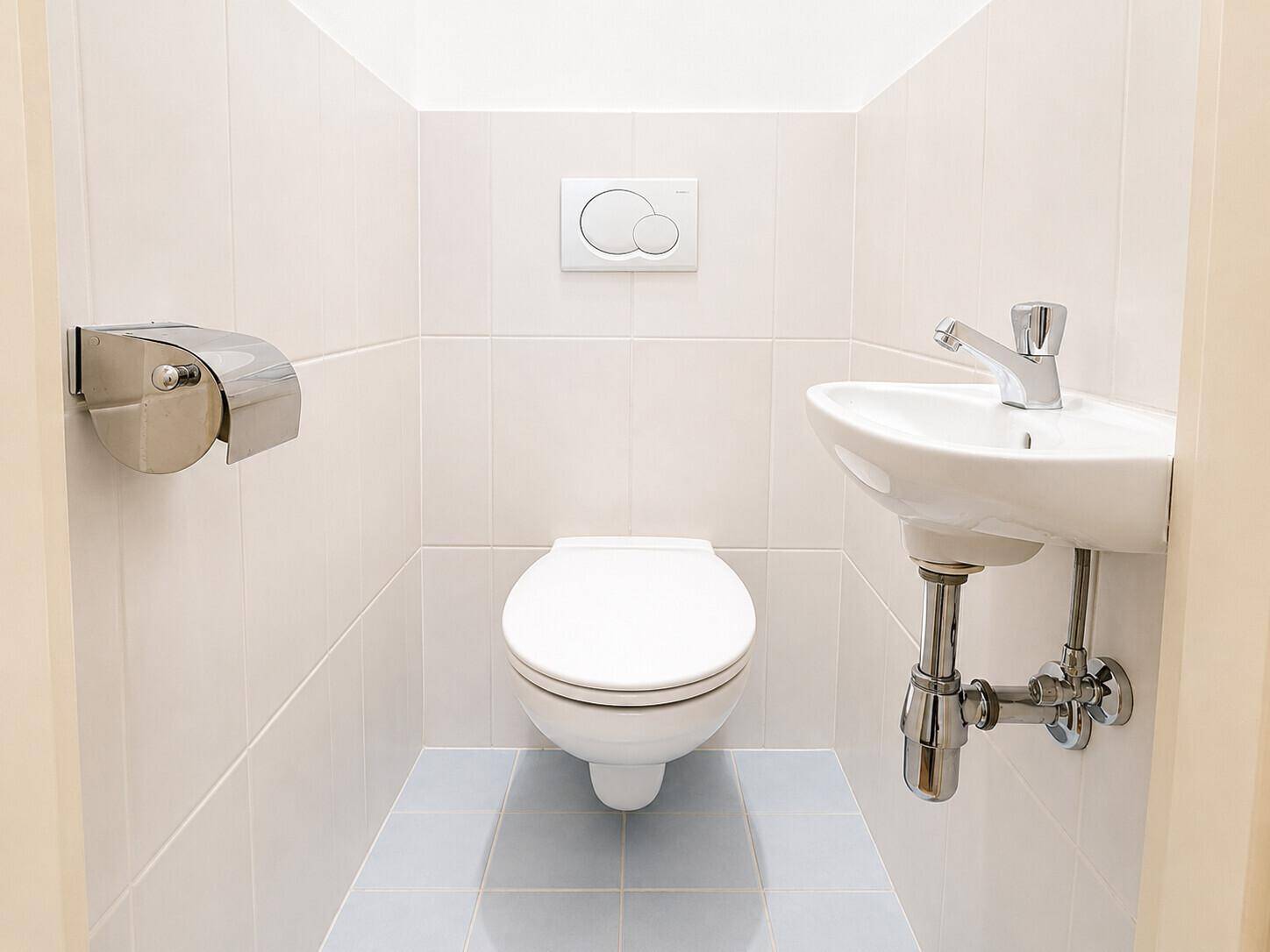 Kleines Gäste-WC mit Wand-WC, Waschbecken und hellen Fliesen.