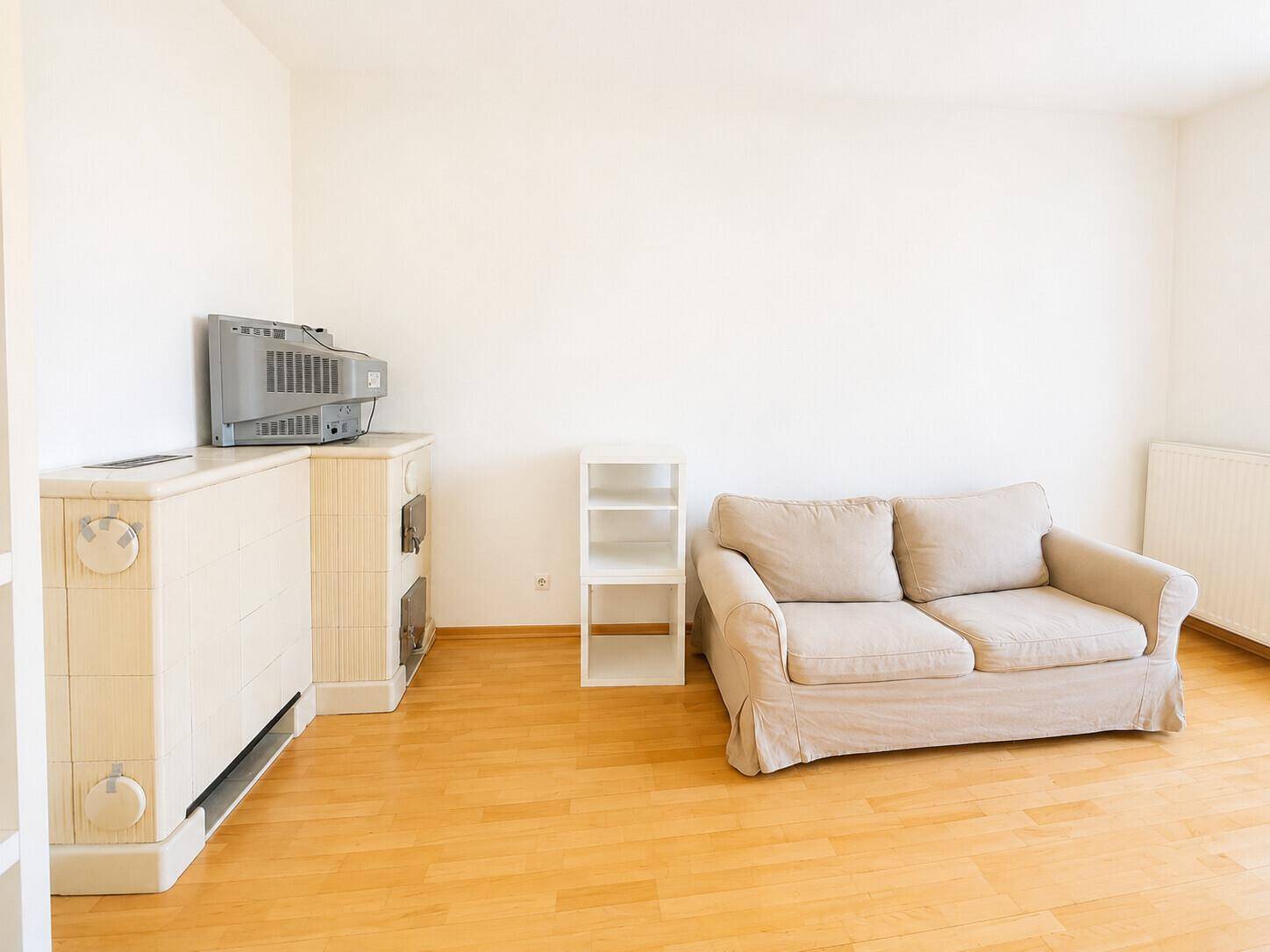 Wohnzimmer mit Parkettboden, Sofa und einem traditionellen Kachelofen.