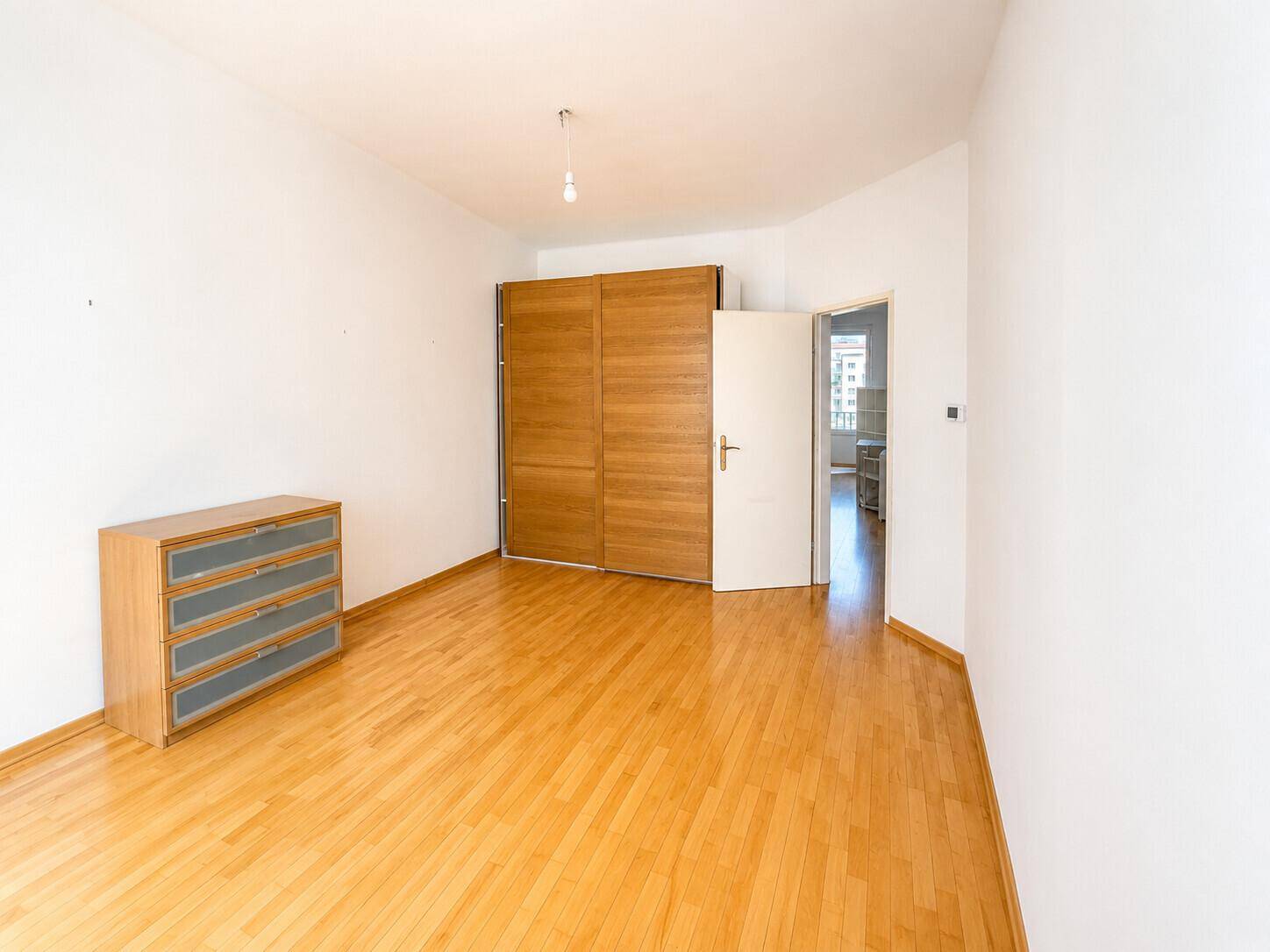Schlafzimmer mit hellem Parkettboden und großem Holzschrank.