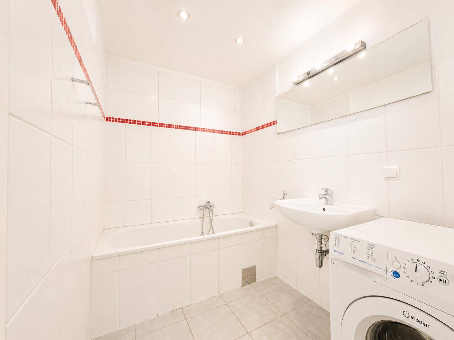 Badezimmer mit Badewanne, Waschbecken, Waschmaschine und roten Akzentfliesen.