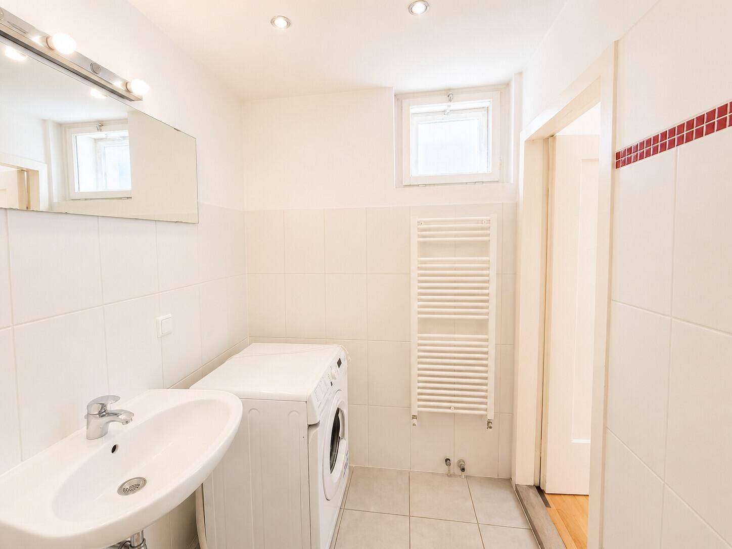 Badezimmer mit Waschmaschine, Waschbecken, Handtuchheizkörper und Fenster.