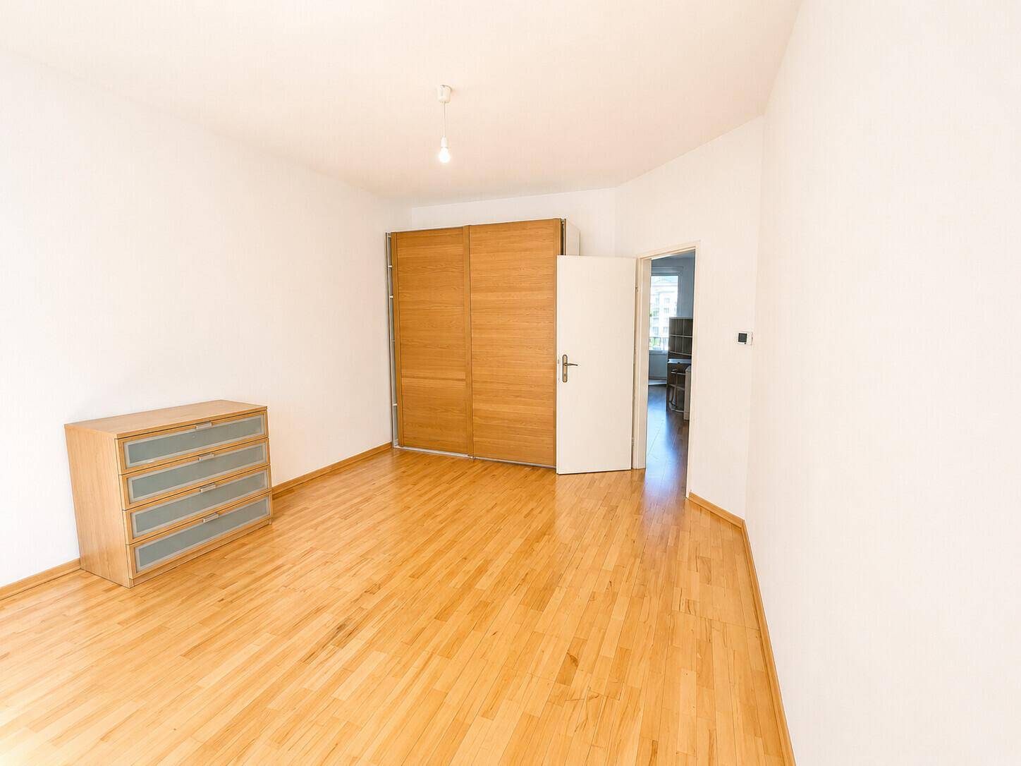 Schlafzimmer mit hellem Parkettboden und großem Holzschrank.
