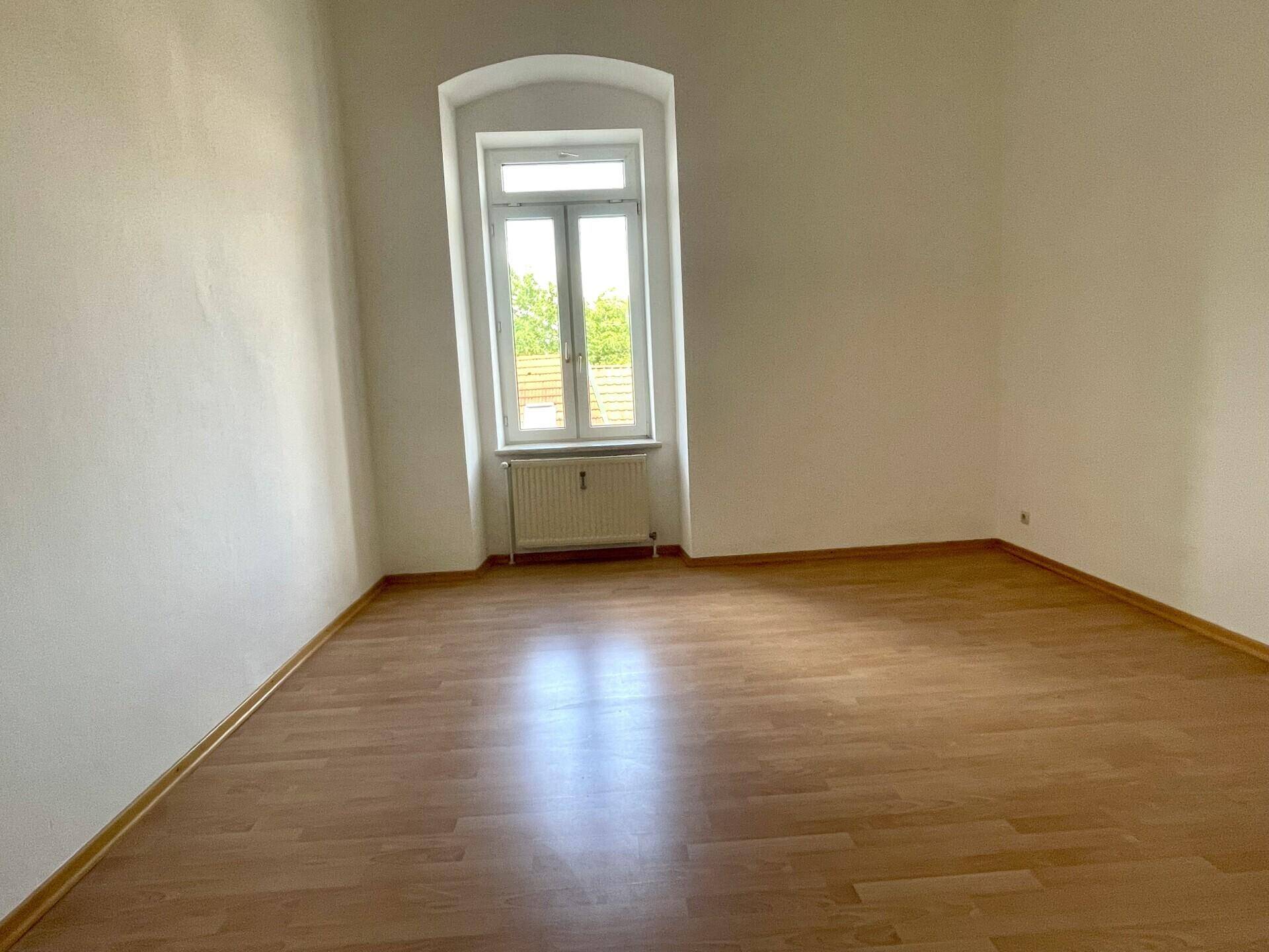 Lichtdurchflutetes Zimmer mit Holzboden und hohem Fenster, vielseitig nutzbar.