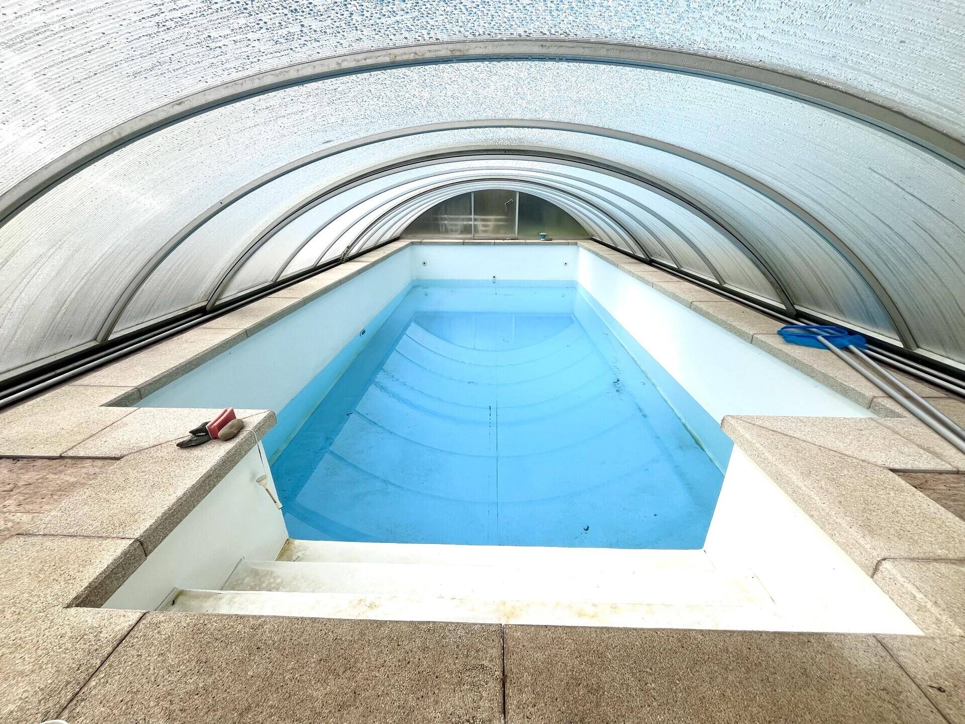 Überdachter Swimmingpool mit klarem Wasser und Steinfliesen am Beckenrand, bereit zur Nutzung.