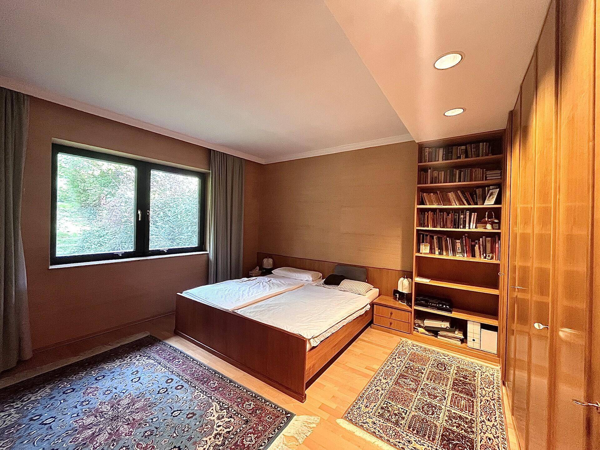 Schlafzimmer mit Doppelbett, Holzboden, Einbauregalen und Blick ins Grüne.