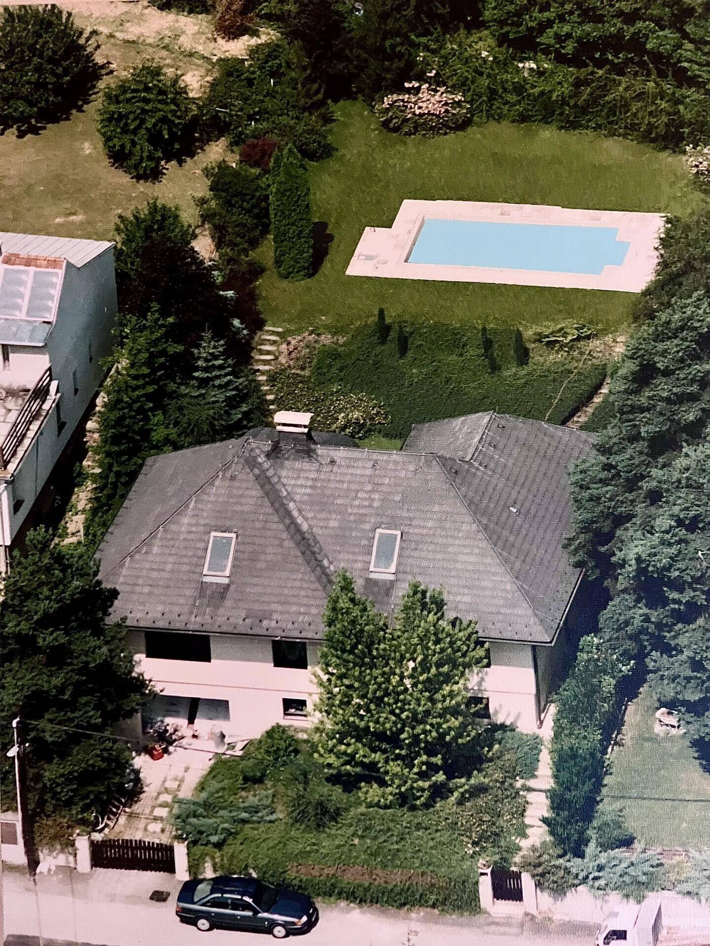 Luftaufnahme eines Hauses mit Satteldach, umgeben von viel Grün und einem Swimmingpool im Garten.