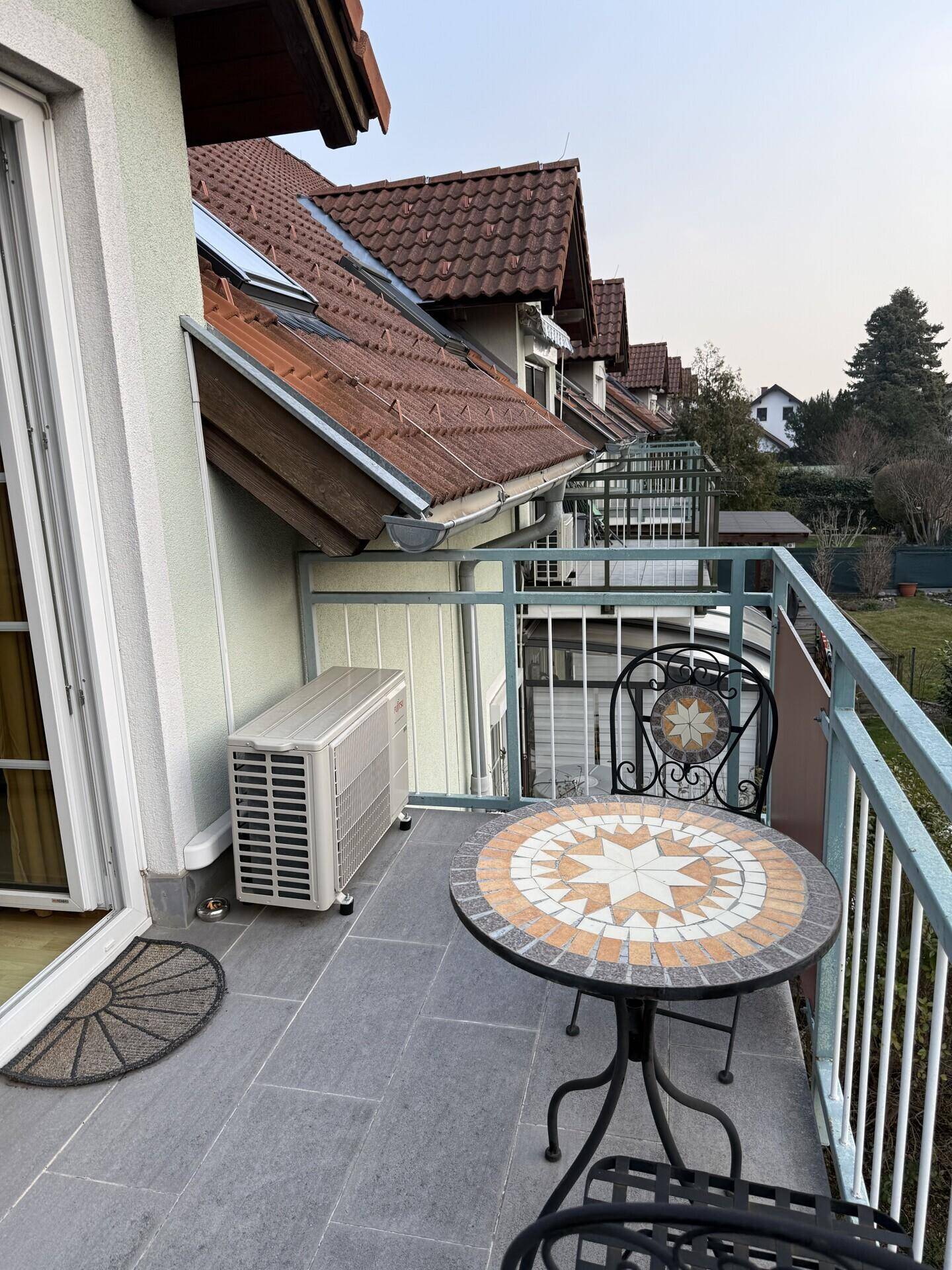 Balkon mit Mosaiktisch, Stühlen und einer Klimaanlage-Außeneinheit an der Fassade.