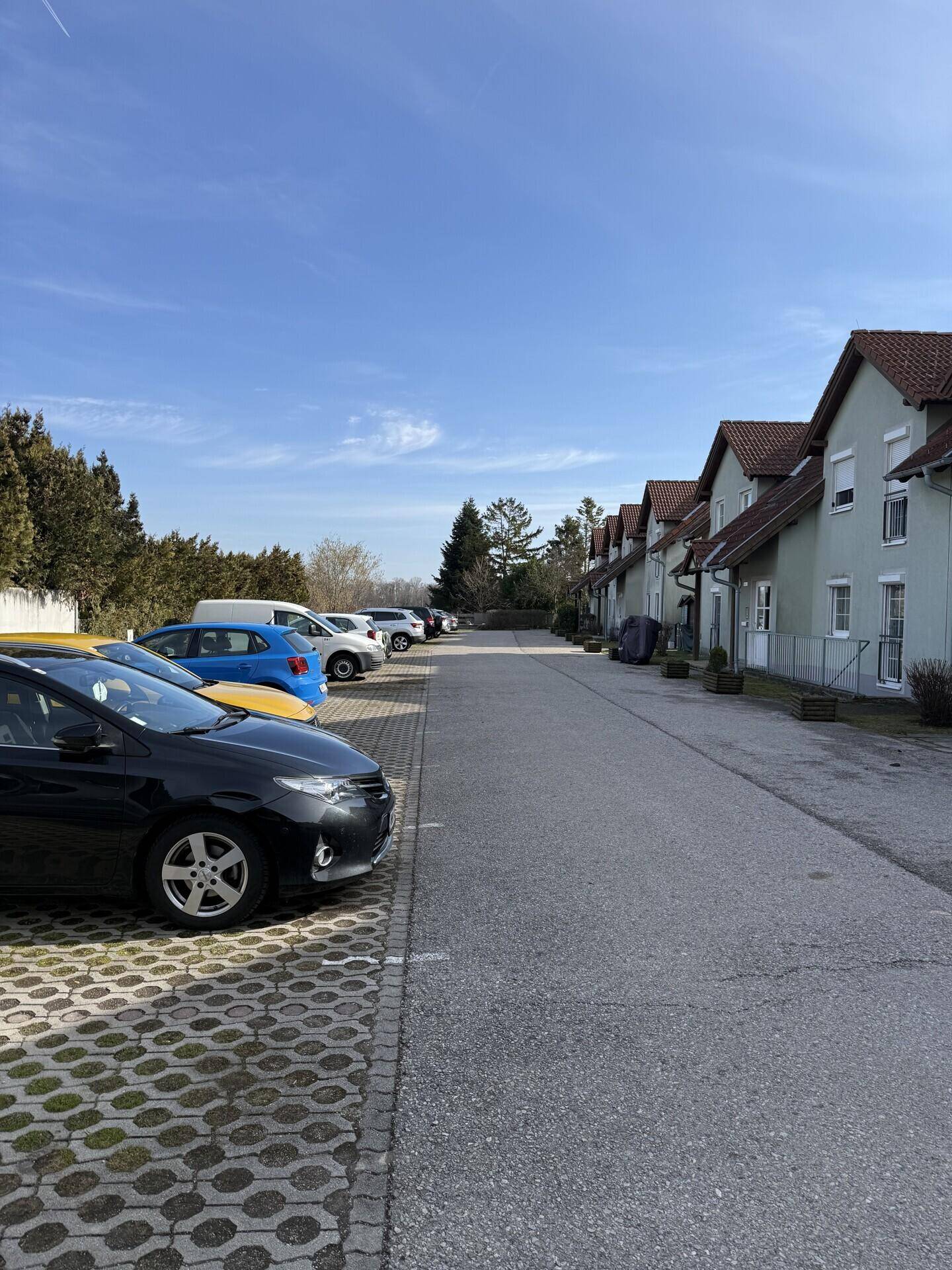 Parkplatz mit mehreren Autos vor einer Reihe von Wohnhäusern unter blauem Himmel.