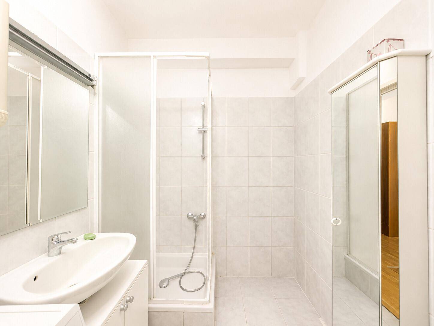 Helles Badezimmer mit Duschkabine, Waschbecken und weißen Fliesen.