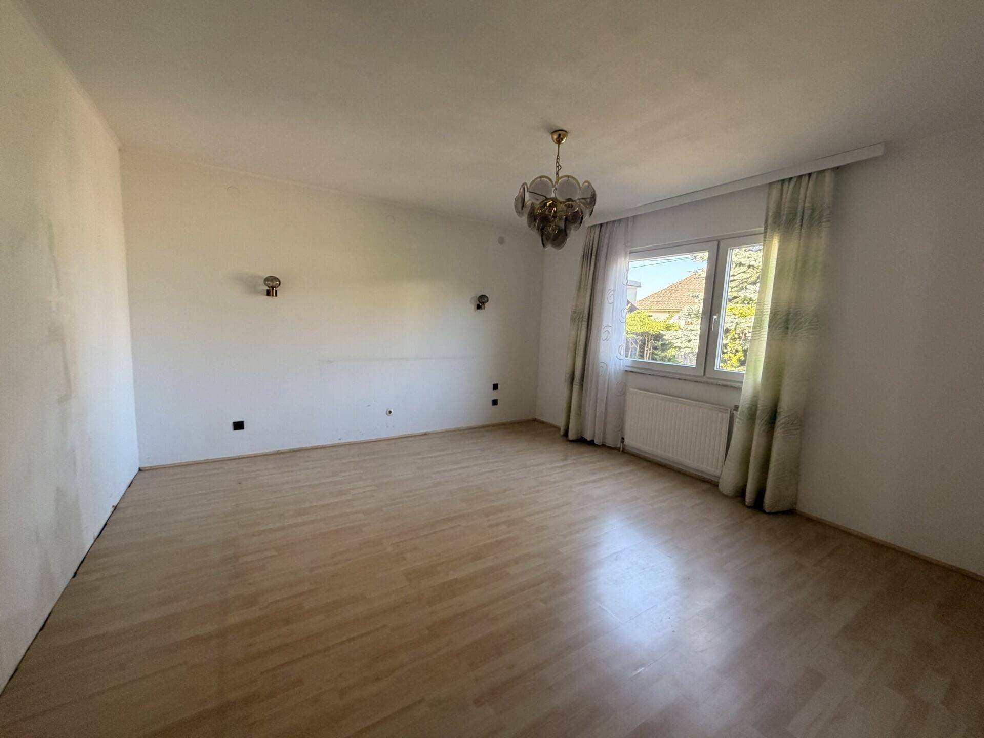 Schlafzimmer mit Laminatboden, Fenster und Blick auf die Umgebung.