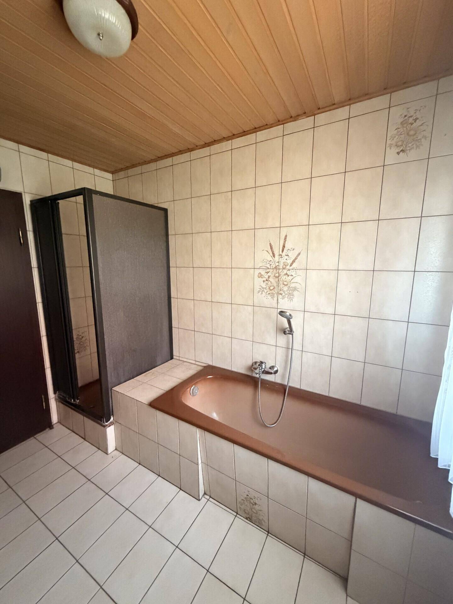 Badezimmer mit Badewanne, Duschkabine, Fliesen und Holzdecke.