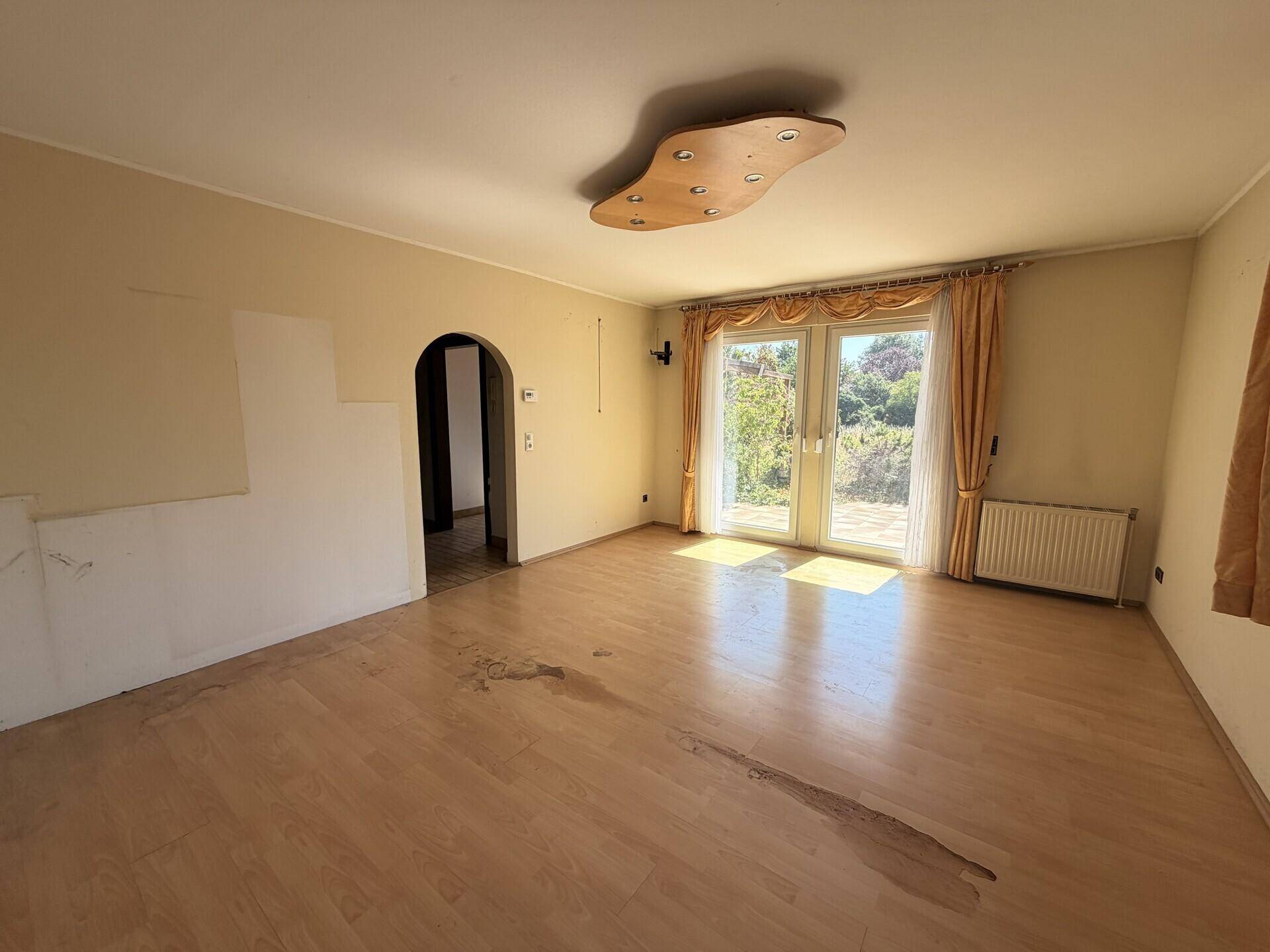 Helles Wohnzimmer mit Laminatboden, Terrassenzugang und Blick ins Grüne.