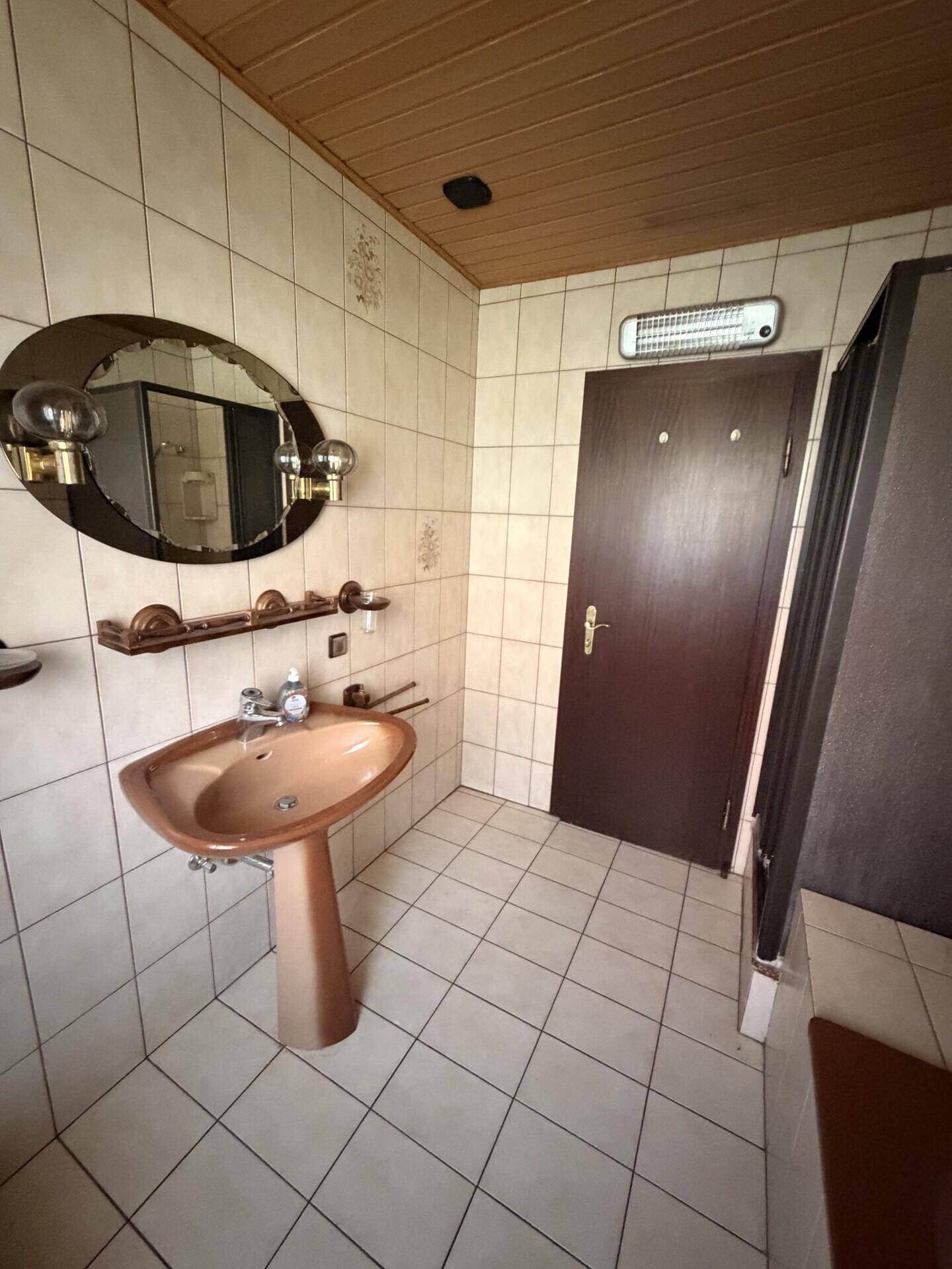 Badezimmer mit Waschbecken, Spiegel, Fliesen und Holzdecke.