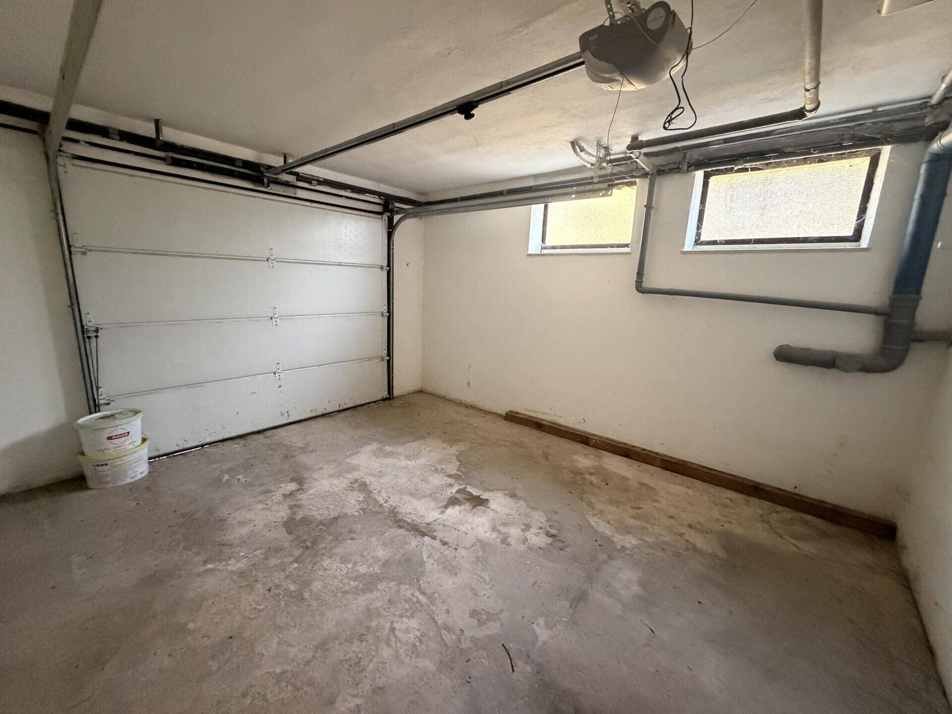 Garage mit Betonboden, Garagentor und zwei kleinen Fenstern.