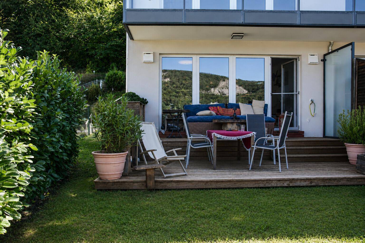 Geräumige Holzterrasse mit Sitzgelegenheiten und direktem Zugang zum grünen Gartenbereich.