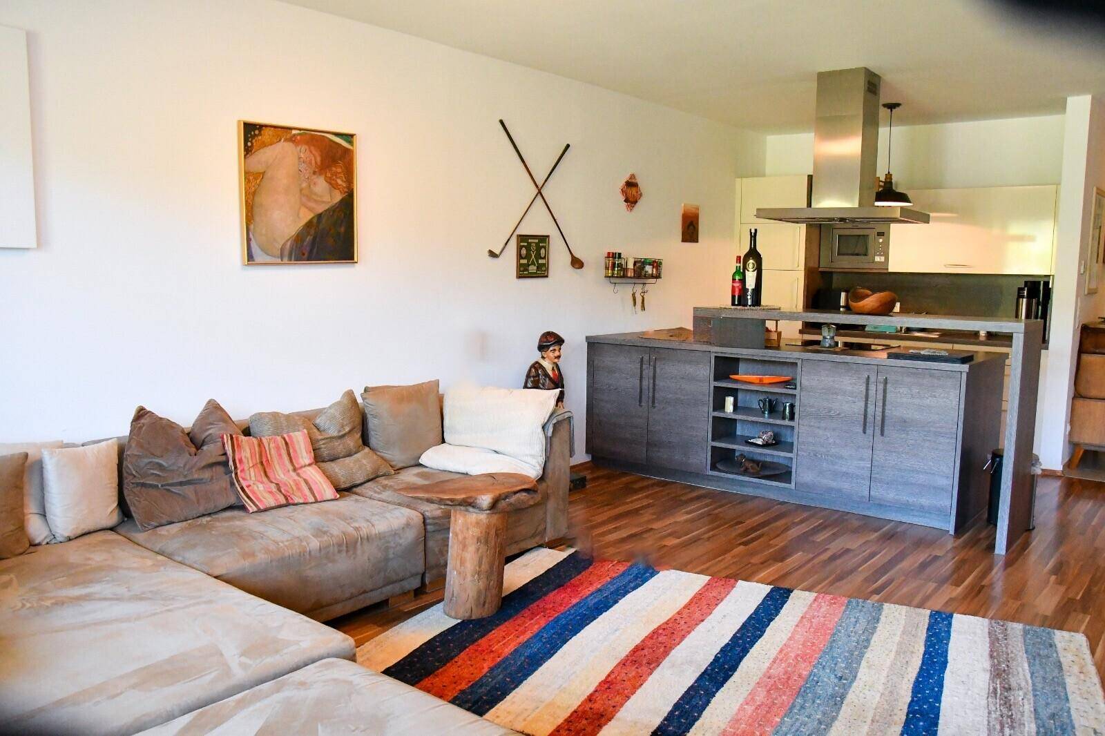 Gemütlicher Wohnbereich mit Sofa, farbigem Teppich und offener Verbindung zur modernen Küche.