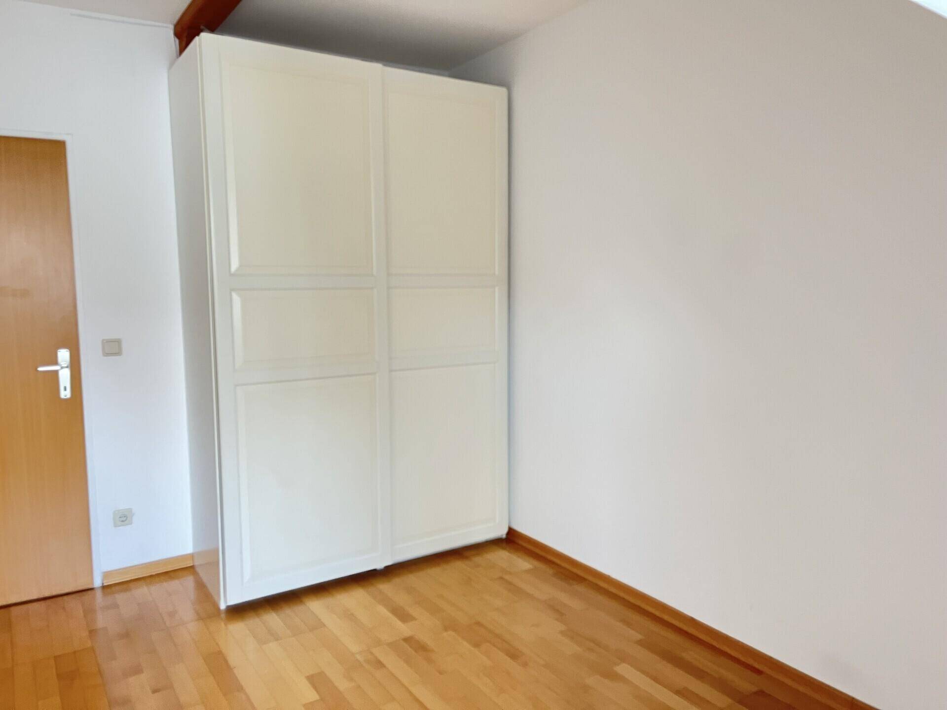 Schlafzimmer mit Parkettboden und weißem Kleiderschrank, helle und freundliche Atmosphäre.