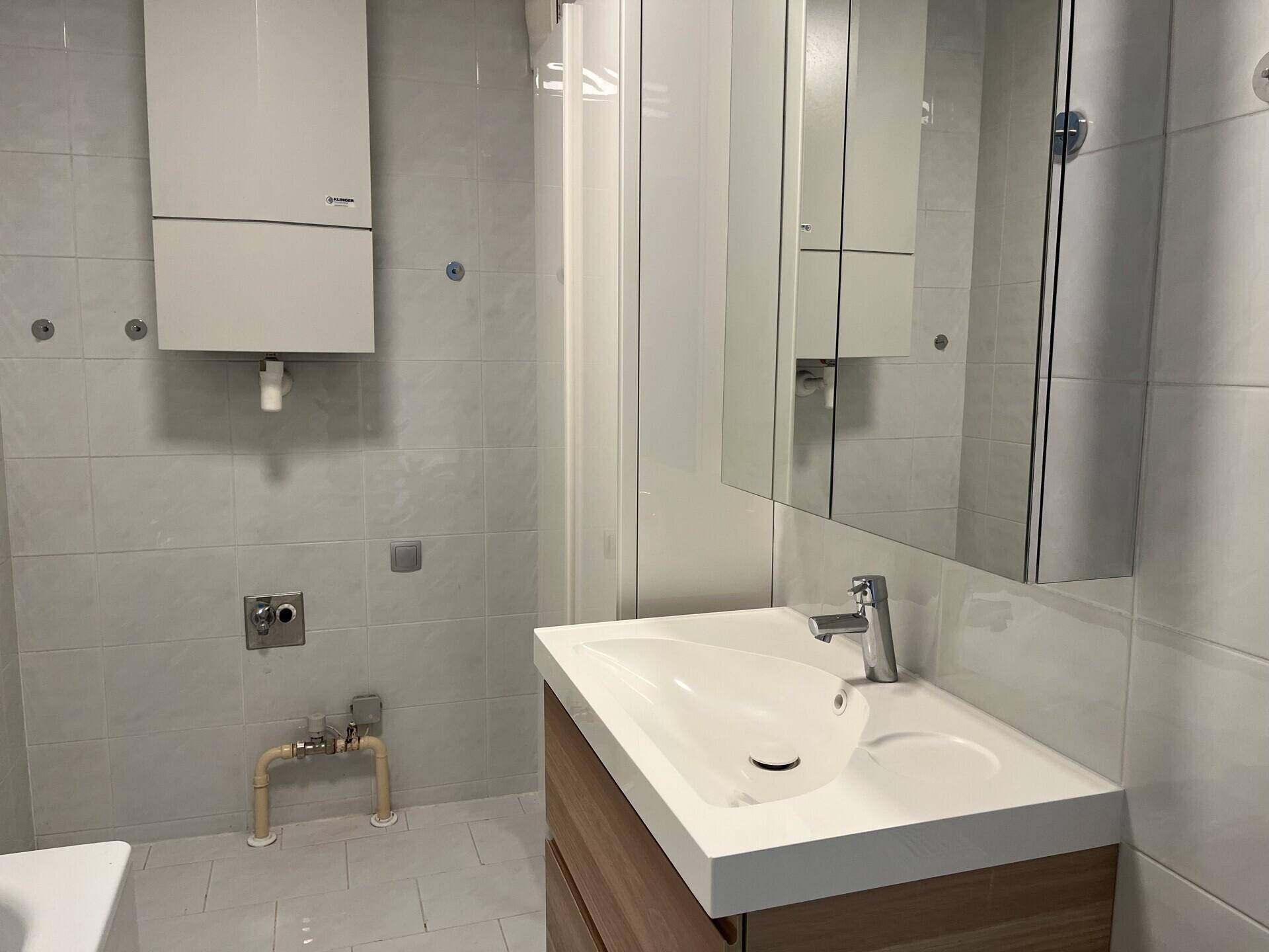Badezimmer mit modernem Waschtisch, Spiegelschrank und Heiztherme an der Wand.
