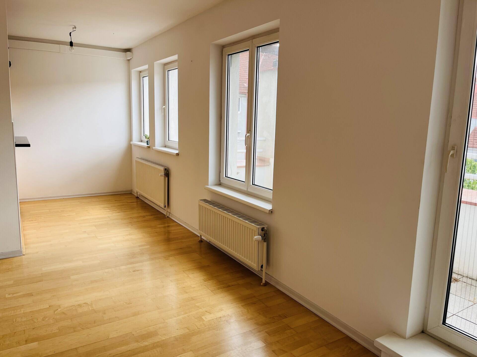 Lichtdurchfluteter Wohnbereich mit Parkettboden, mehreren Fenstern und Heizkörpern.