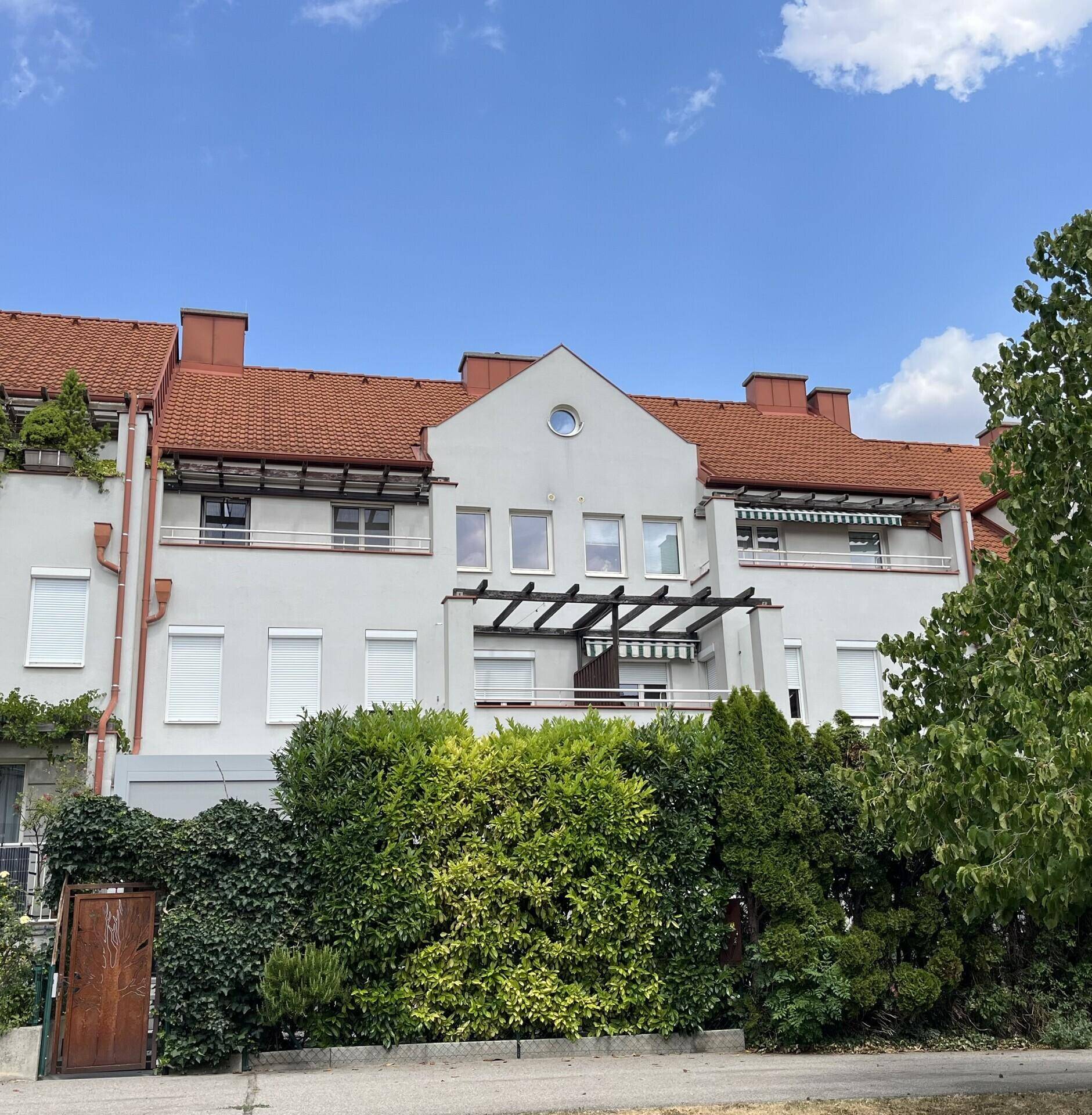 Wohngebäude mit rotem Ziegeldach, grüner Hecke und Pergola-Strukturen an der Fassade.