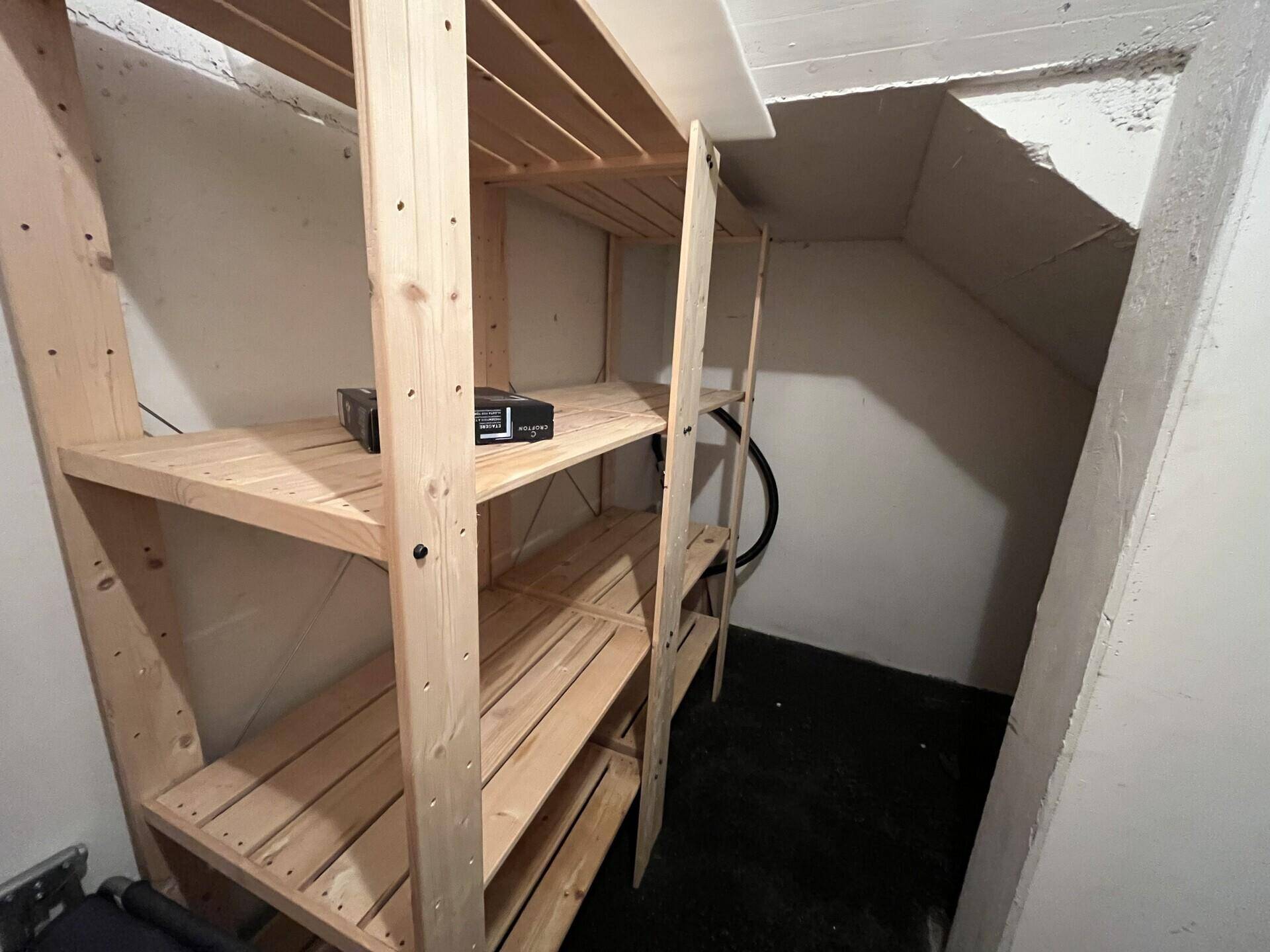 Einfacher Abstellraum mit Holzregalen und Betonwänden, ideal für zusätzlichen Stauraum.