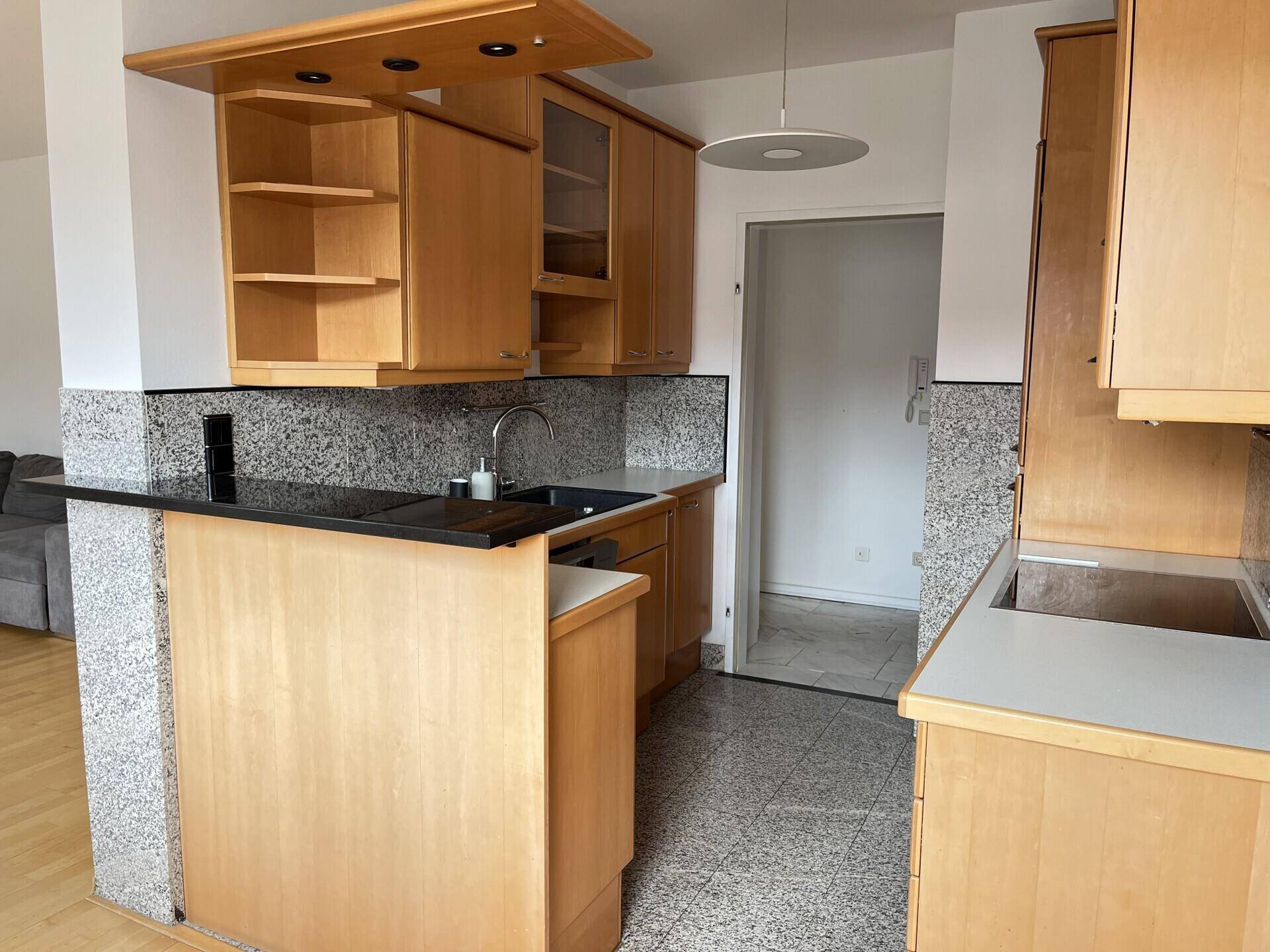 Offene Küche mit Thekenbereich, Holzschränken und Granit-Arbeitsplatte, angrenzend an den Wohnbereich.