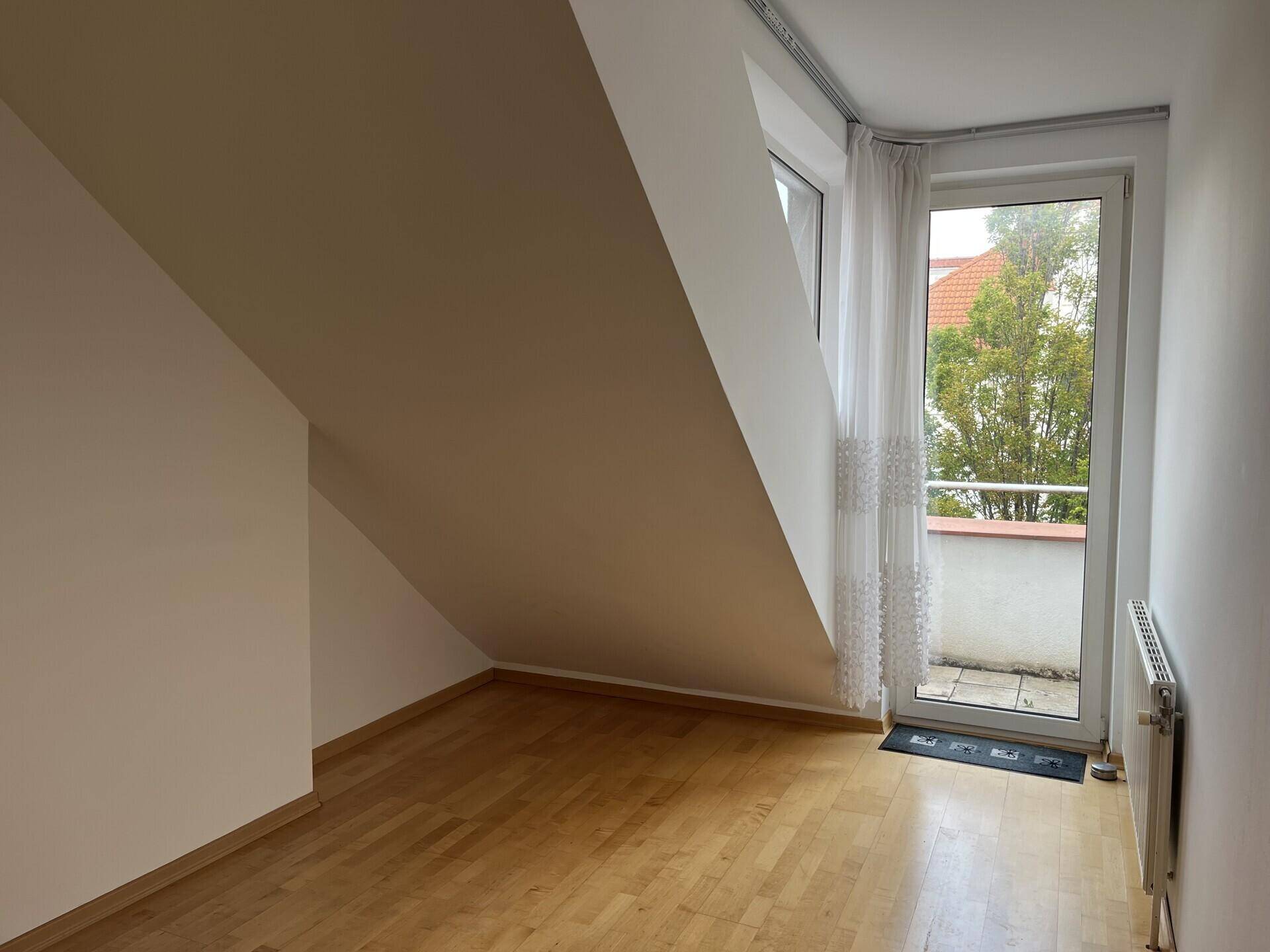 Schlafzimmer im Dachgeschoss mit Parkettboden, Dachschräge und Fenstertür zum Balkon.