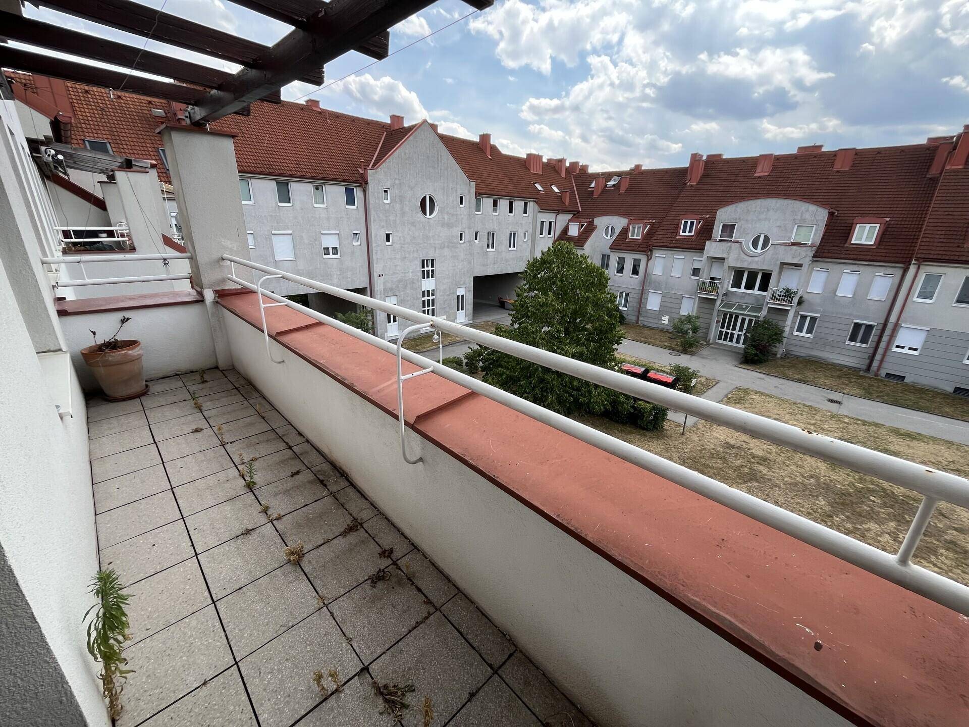 Balkon mit Fliesenboden und Blick auf den Innenhof mit weiteren Wohngebäuden.