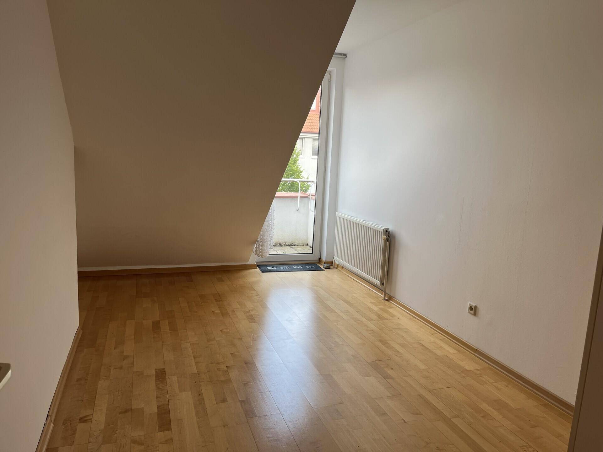 Schlafzimmer im Dachgeschoss mit Parkettboden, Dachschräge und Zugang zu einem kleinen Balkon.