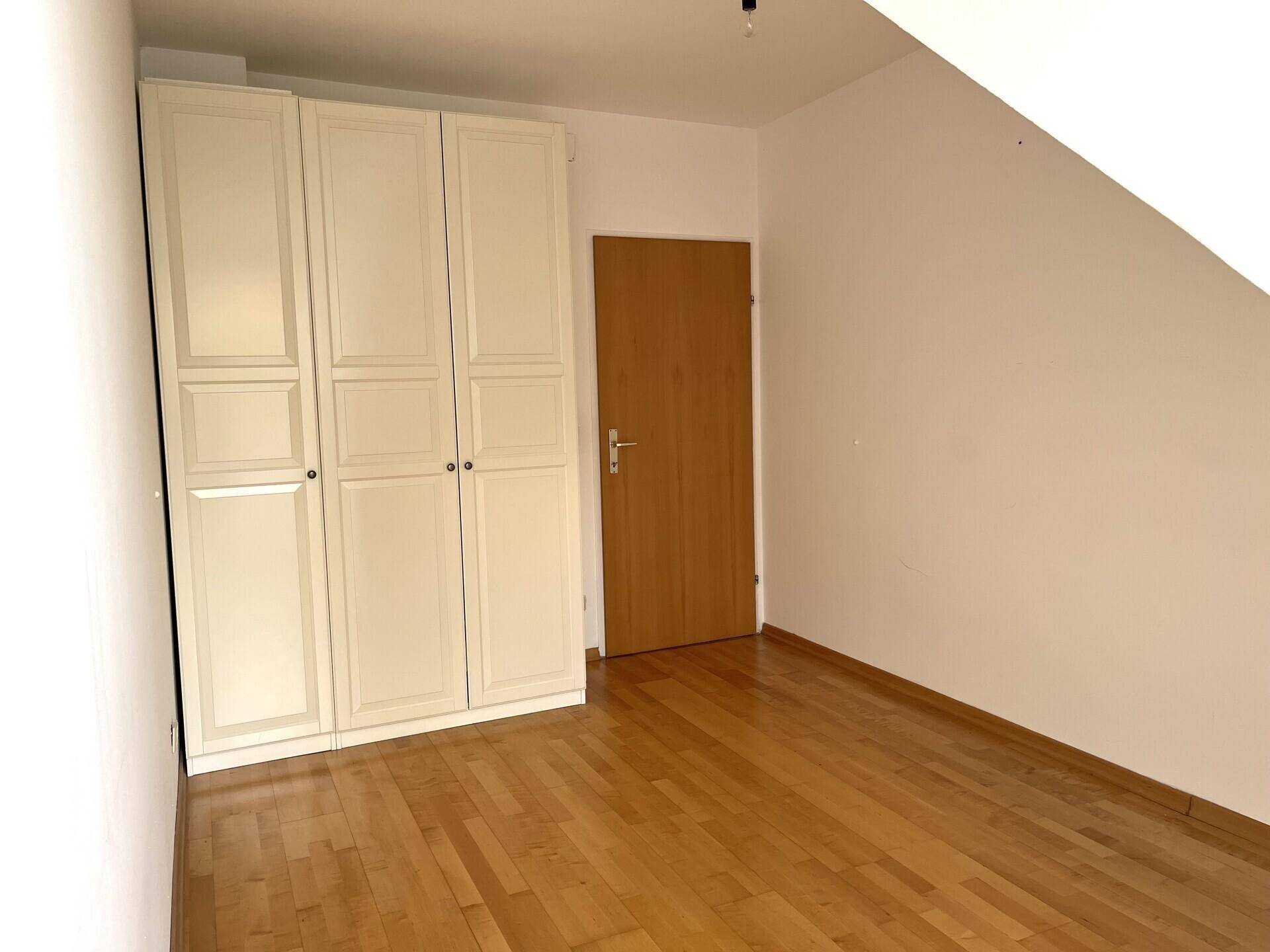 Schlafzimmer im Dachgeschoss mit Parkettboden und großem weißen Kleiderschrank.