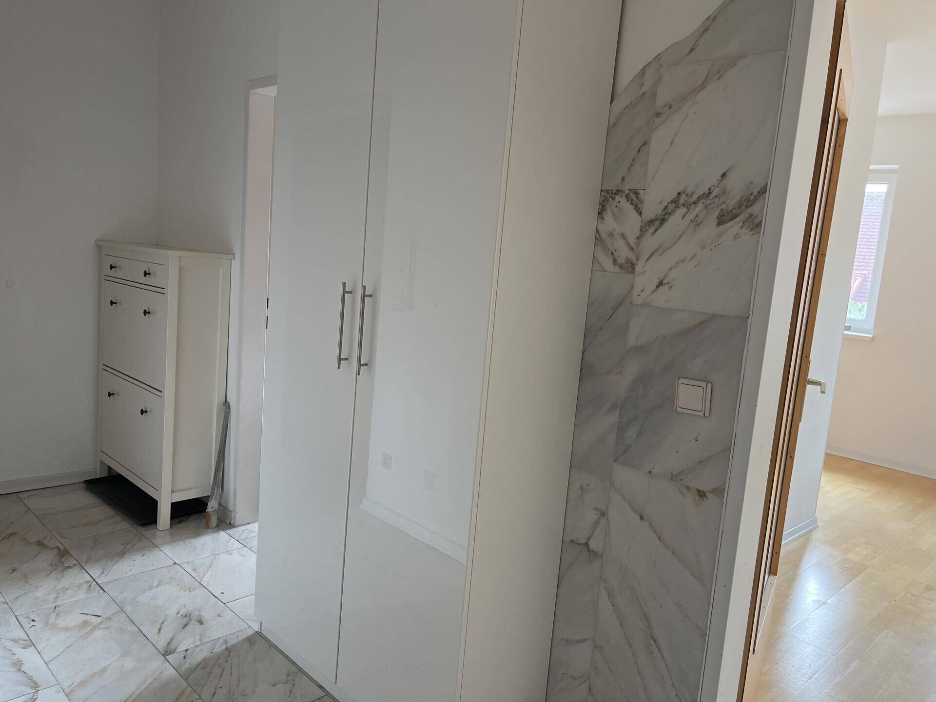 Heller Flur mit Marmorfliesen, weißem Schrank und Schuhregal, gut gepflegt.