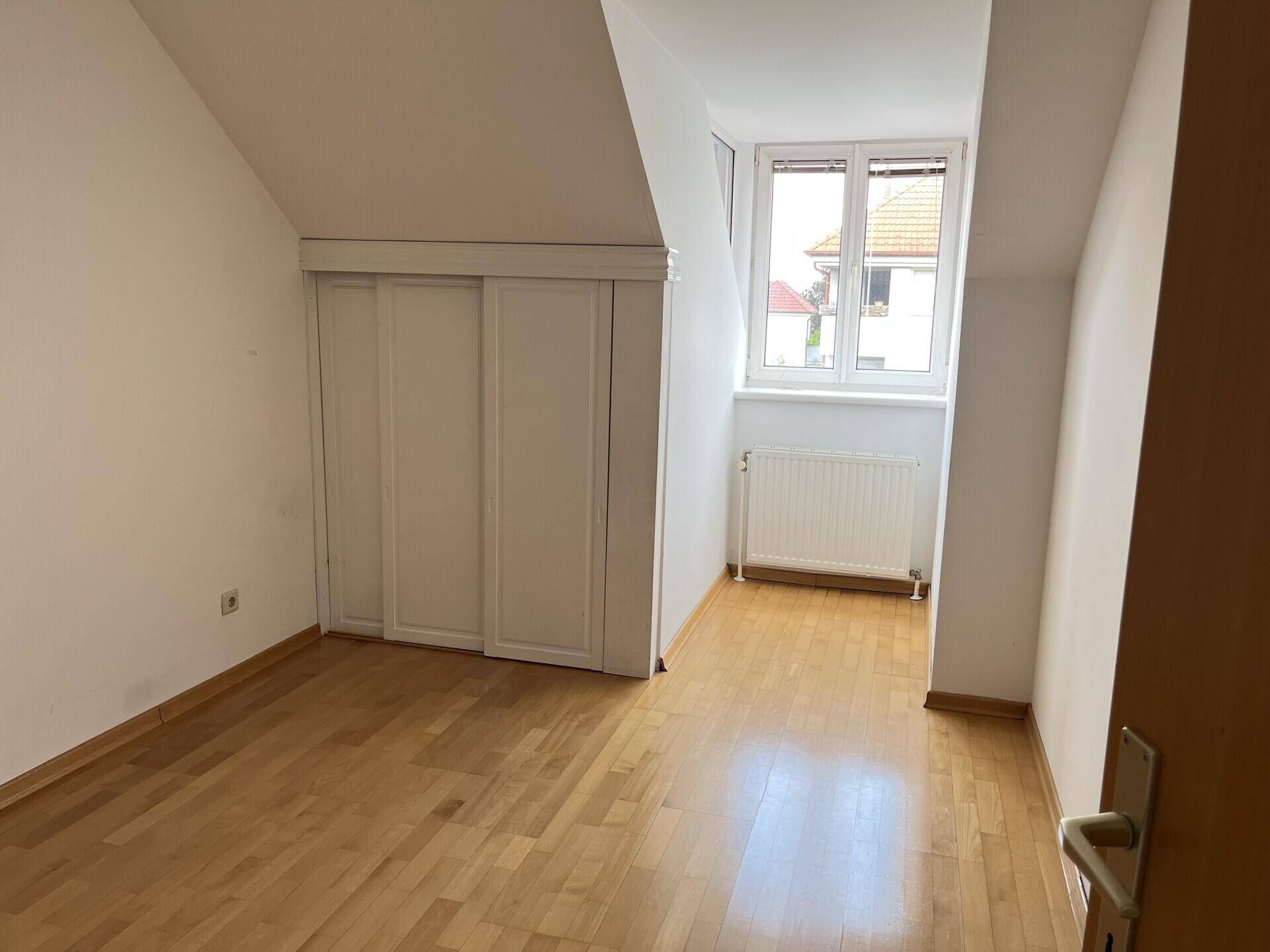 Schlafzimmer im Dachgeschoss mit Parkettboden, Einbauschrank und Fenster mit Ausblick.