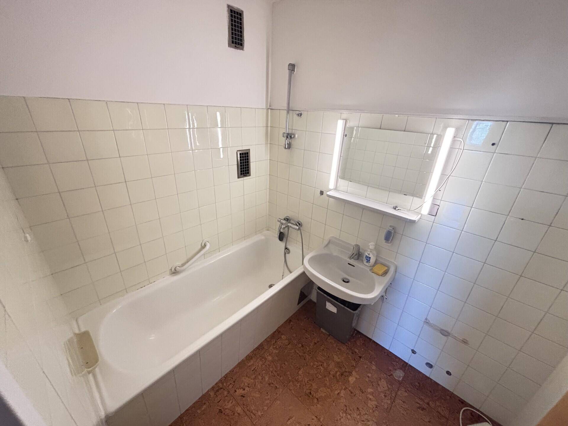 Badezimmer mit Badewanne, Waschbecken, Spiegel und weißen Fliesen, im Stil der 80er Jahre.