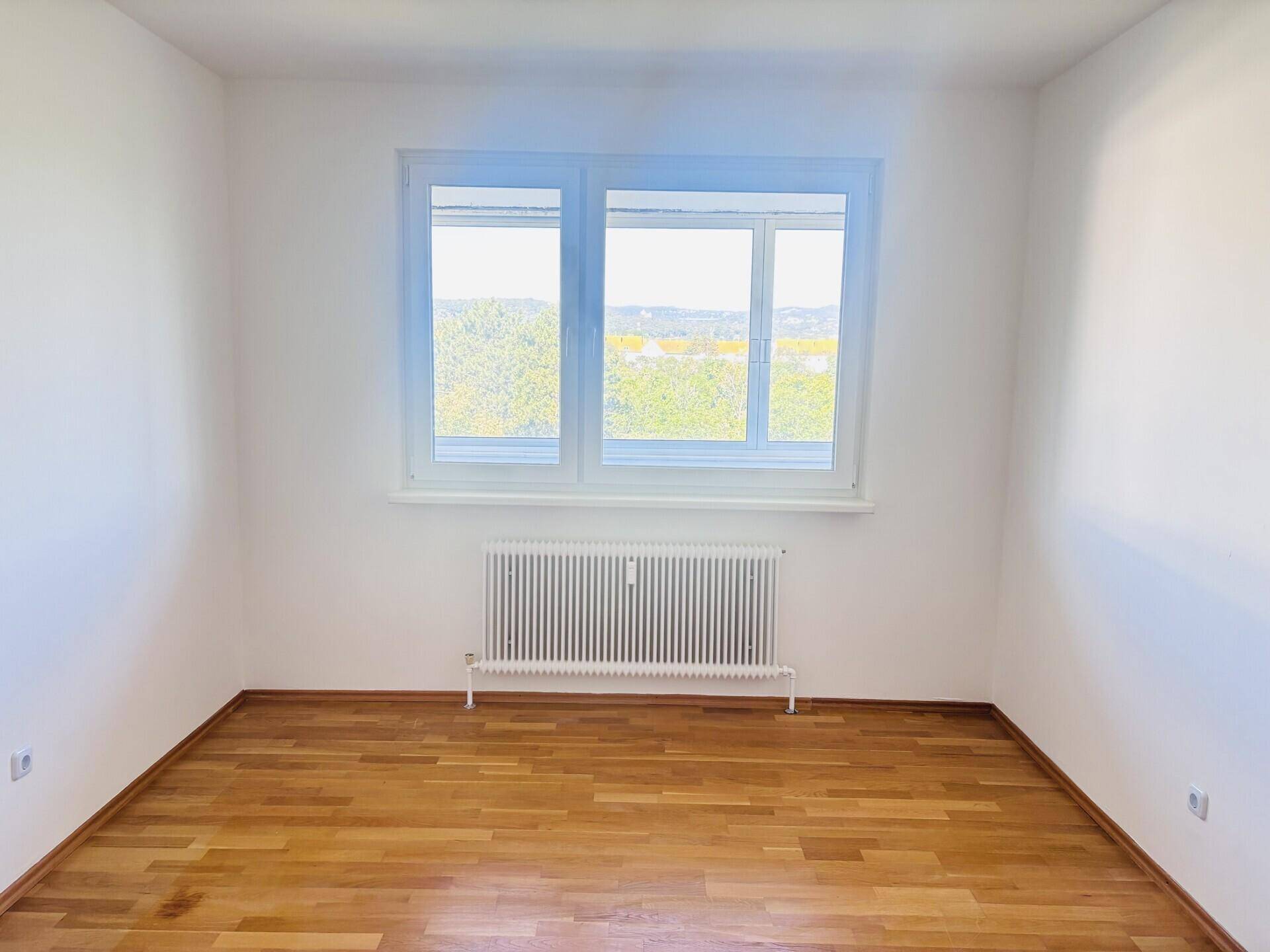 Helles Zimmer mit Parkettboden, weiß gestrichenen Wänden und einem großen Fenster.
