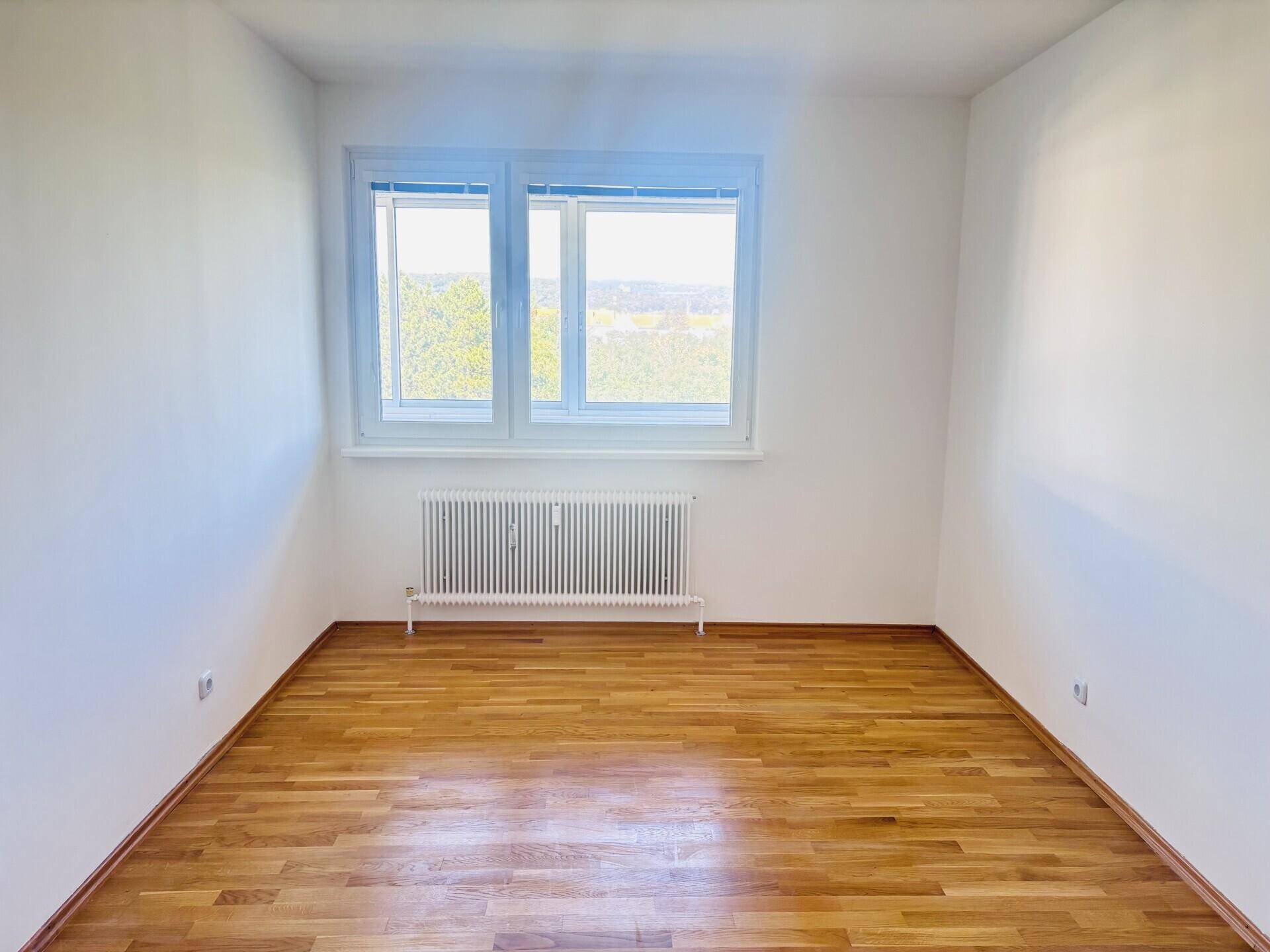 Leeres Schlafzimmer mit hellem Parkettboden, weiß gestrichenen Wänden und einem Fenster.