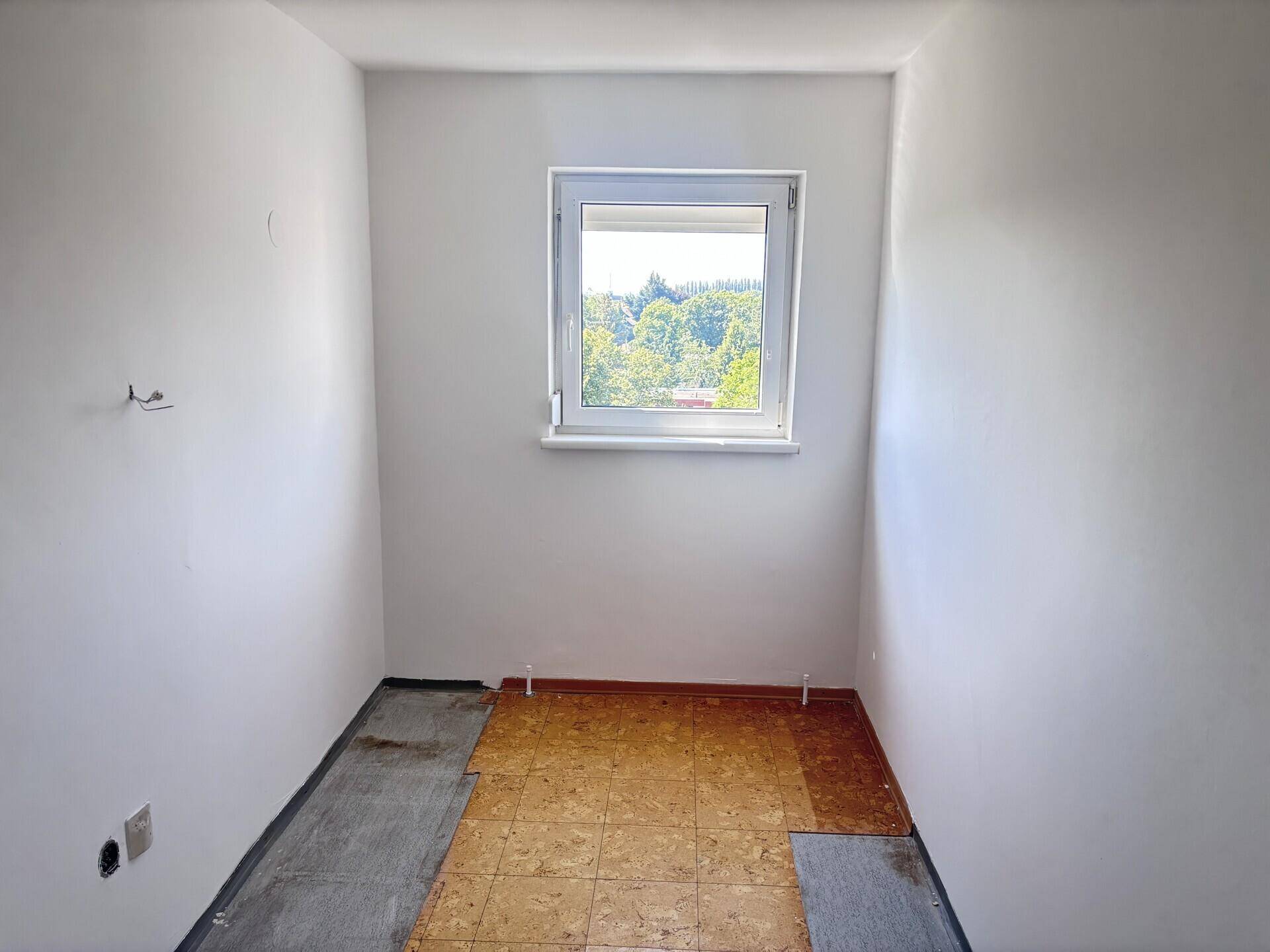 Kleiner Raum mit Fenster, weißen Wänden und teilweise entferntem Bodenbelag, bereit zur Renovierung.