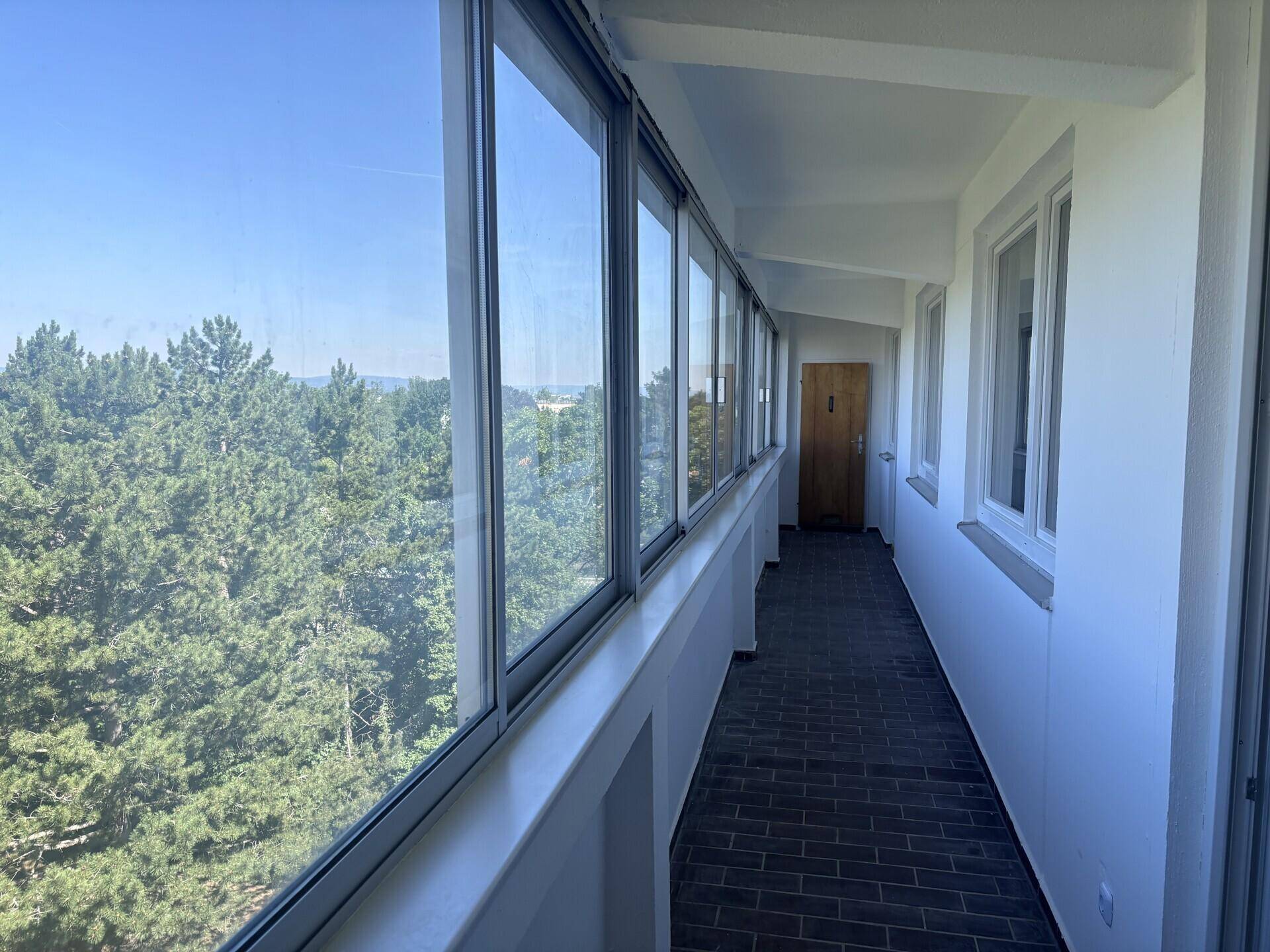 Langer, verglaster Loggia-Bereich mit dunklem Fliesenboden und weitem Blick ins Grüne.