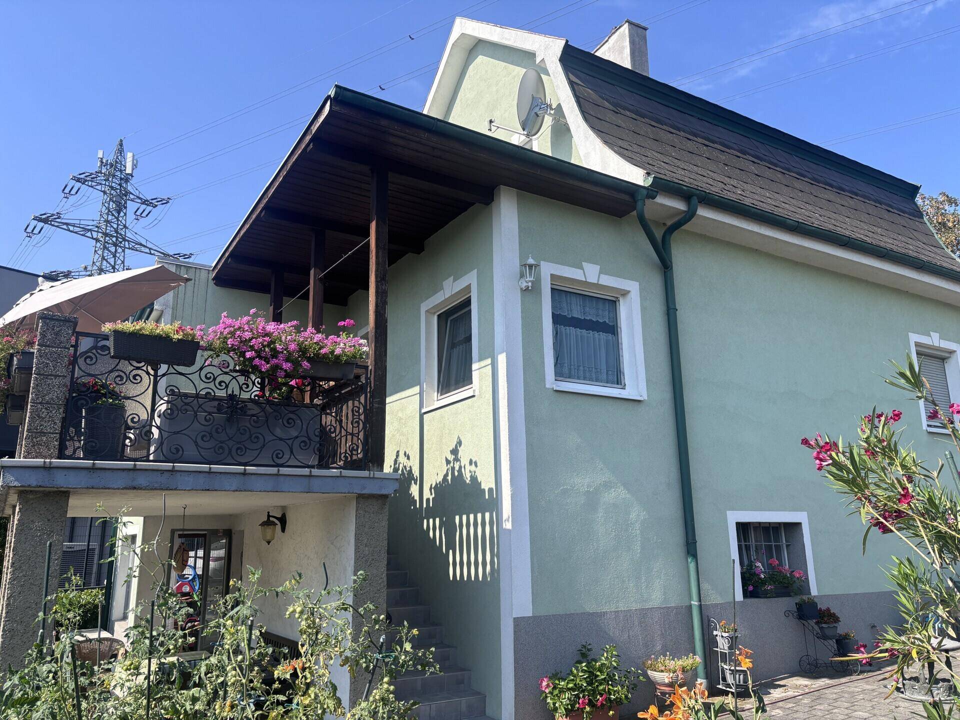 Charmantes Haus mit Balkon, blühenden Blumenkästen und Mansarddach in sonniger Lage.