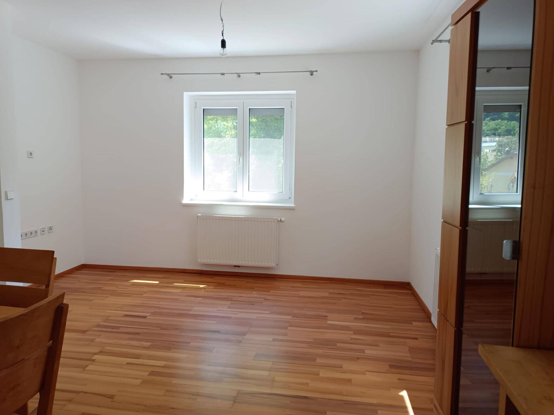 Heller Wohnbereich mit Holzfußboden, großem Fenster und Blick ins Grüne.